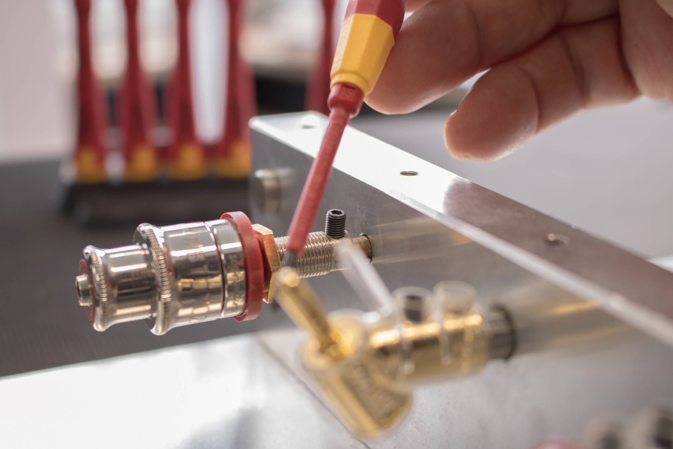 A hand connects a red and yellow cable to a metal connector on a technical device, potentially for electronics work.