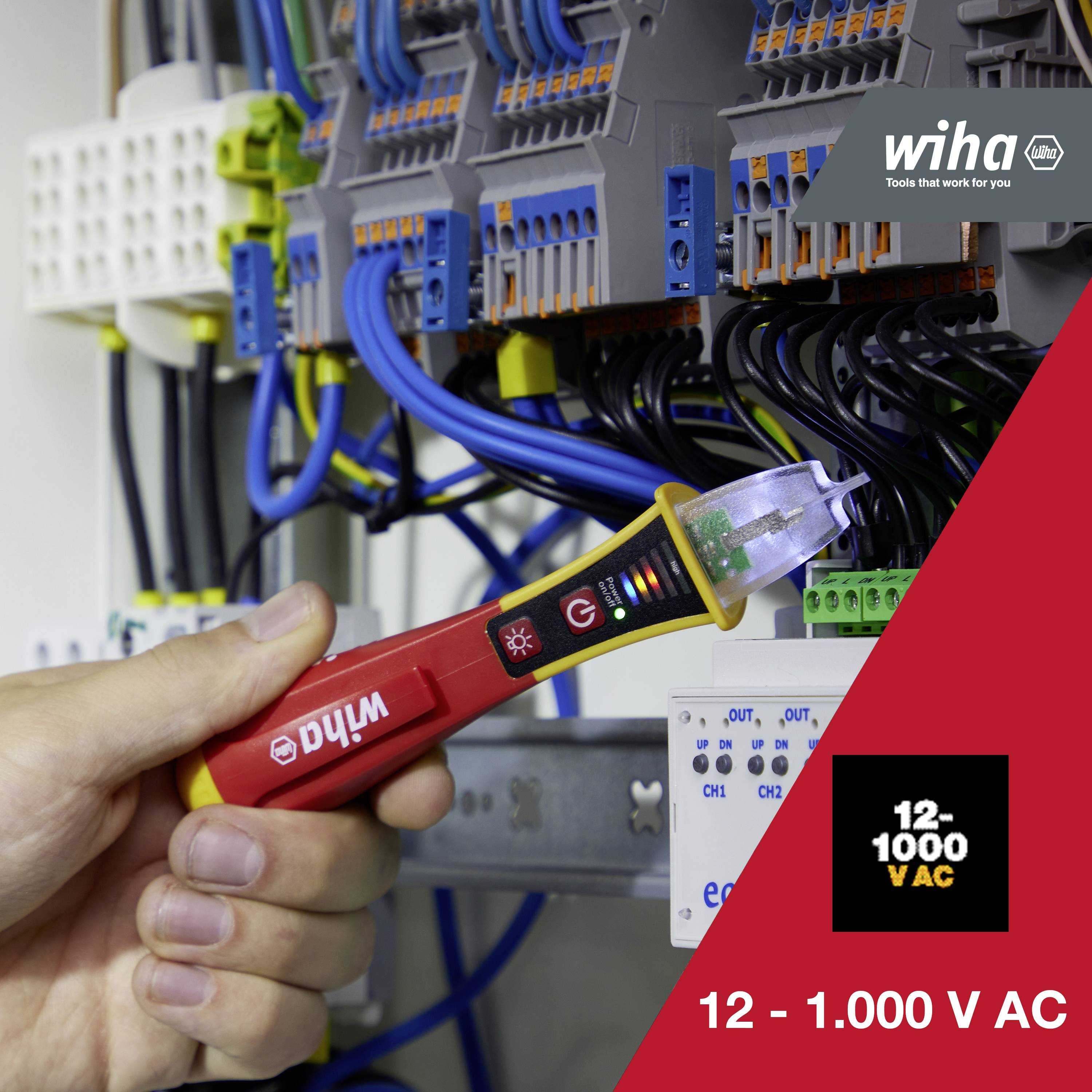 A hand is holding a voltage tester in front of an electrical switchboard with numerous cables, the tester indicating a voltage range of 12 - 1,000 V AC.