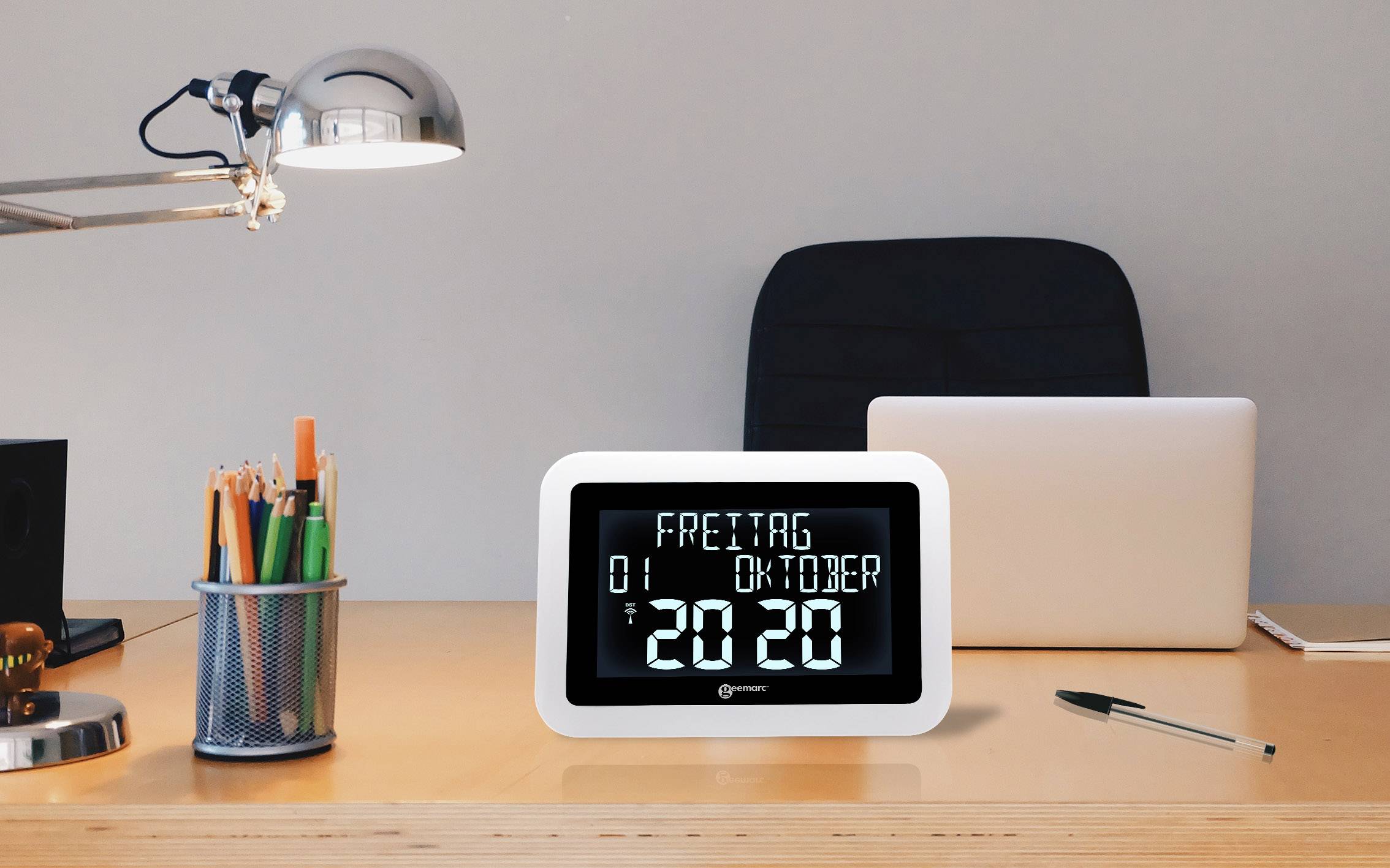A digital calendar on a desk displays 'Friday, 1st October, 20:20'. Next to it are a lamp, pens and a laptop.