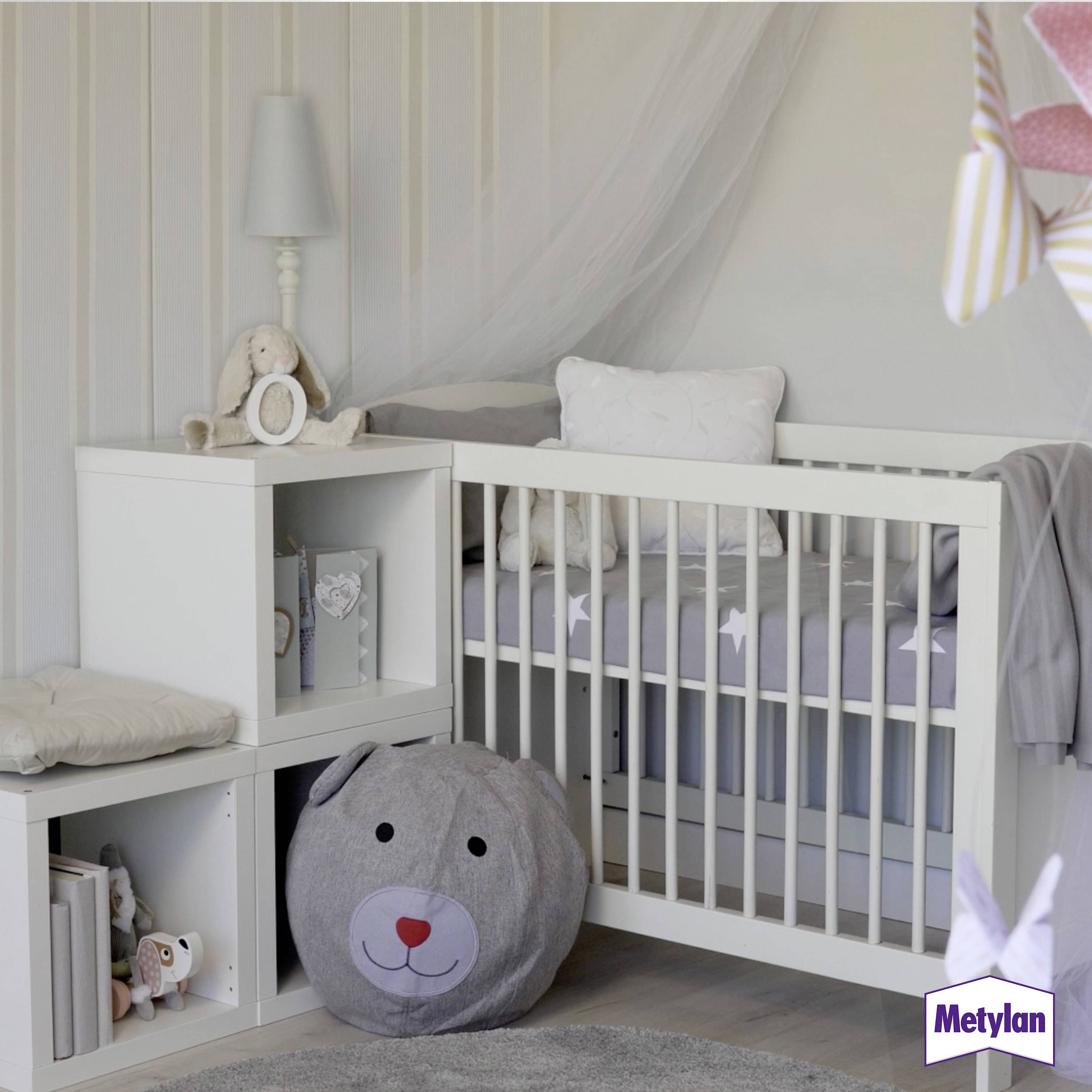 A cozy nursery with a white crib, teddy bear cushion, and stuffed bunny on a shelf. Soft gray and light neutral tones.
