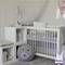A cozy nursery with a white crib, teddy bear cushion, and stuffed bunny on a shelf. Soft gray and light neutral tones.