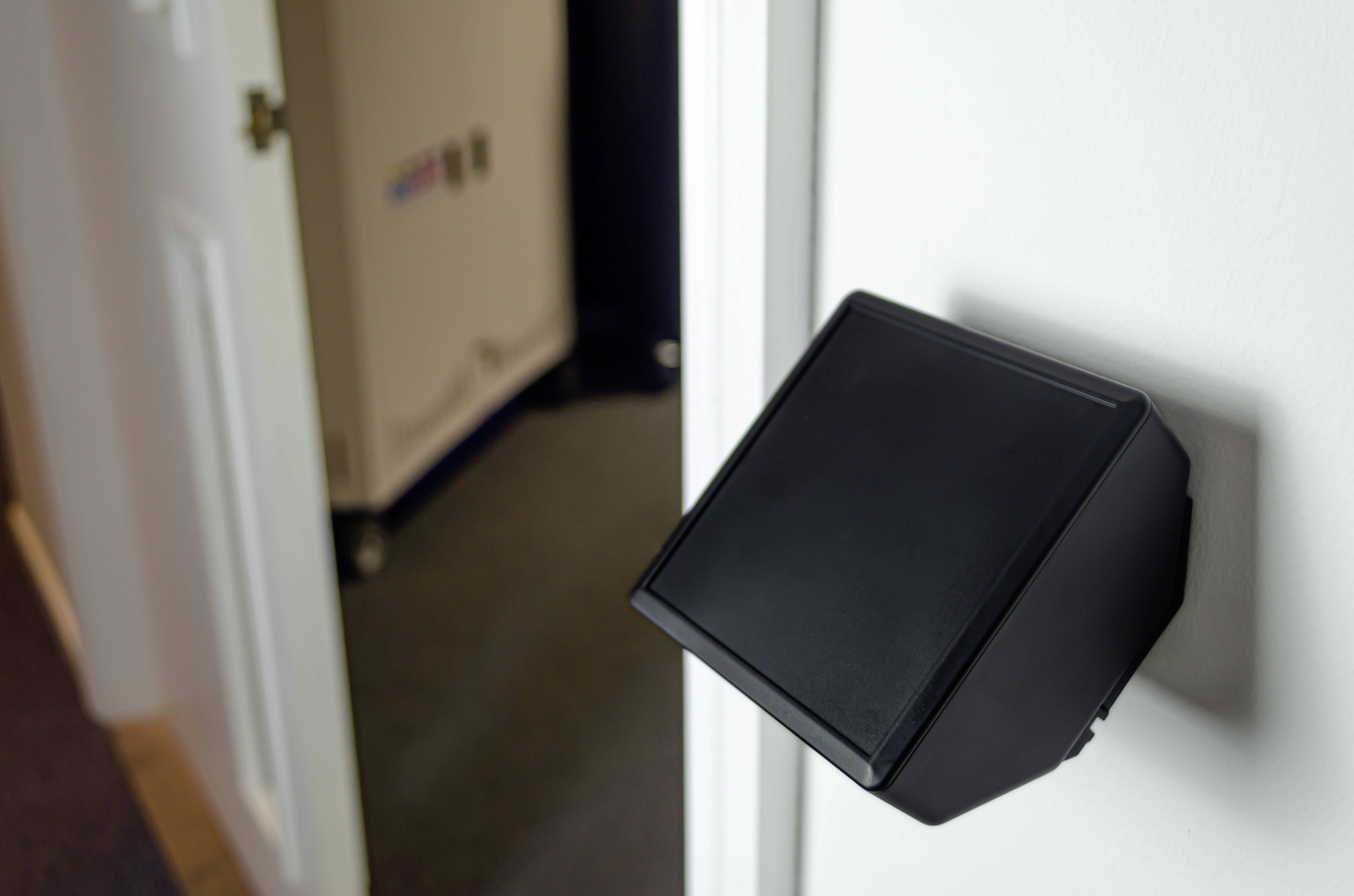 A black card reader is mounted on the wall beside an open door. In the background, a carpeted room can be seen.