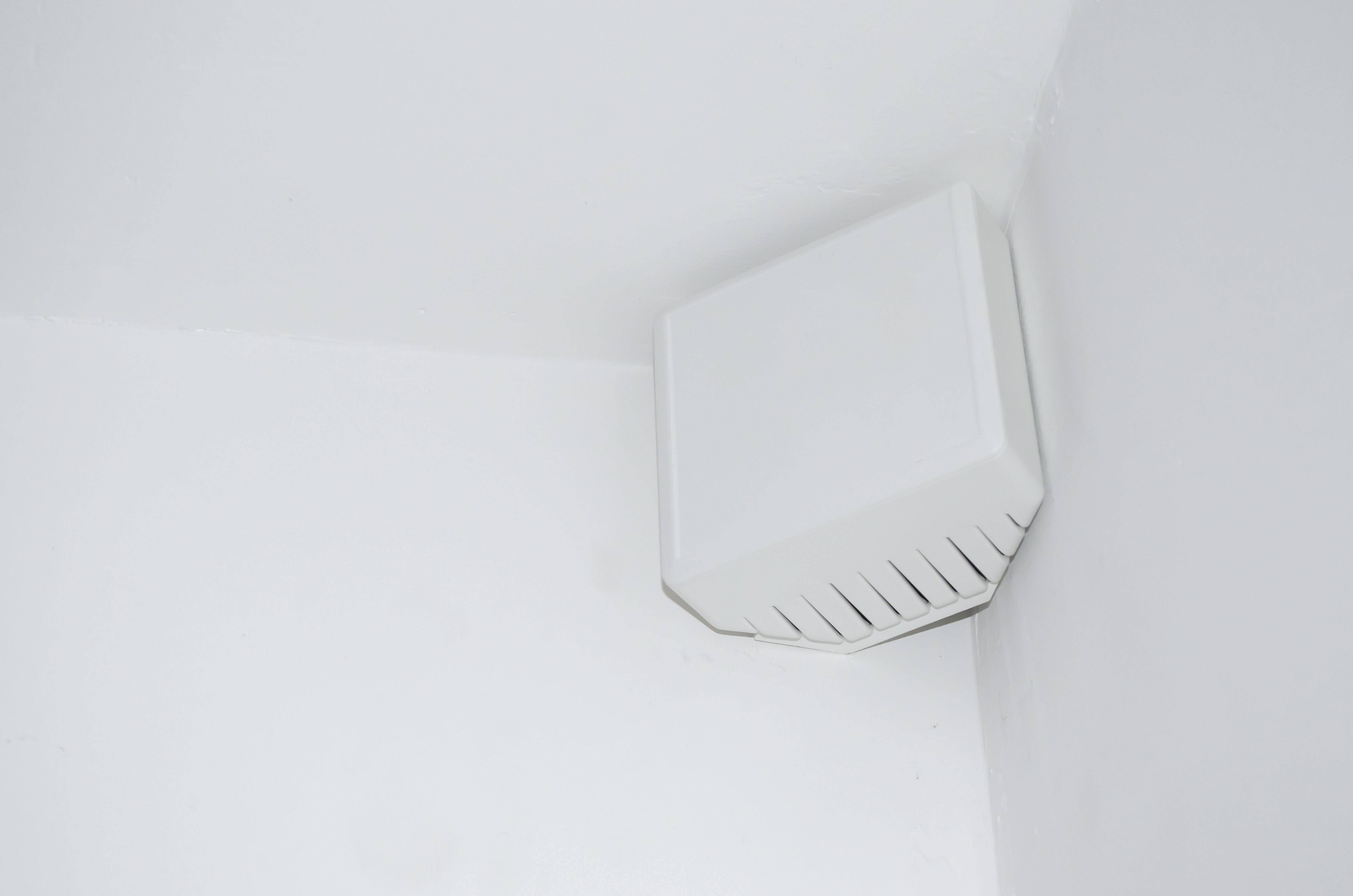 A white speaker is mounted in the corner of a white wall.