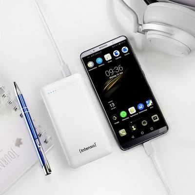 'Power bank and smartphone with charging indicator, connected by cable on a desk with notebook, pen and headphones.'
