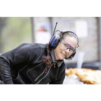A person wearing safety glasses and a headset is smiling while working outside.