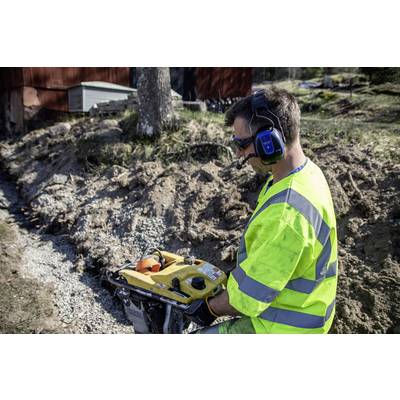 A worker in yellow protective clothing and ear protection is operating a construction machine outdoors to process earth and gravel on a plot of land.