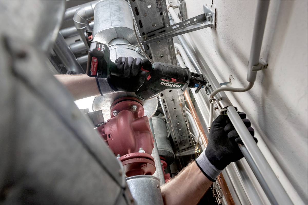 A person wearing work gloves is repairing pipelines with an electric tool in an industrial setting.