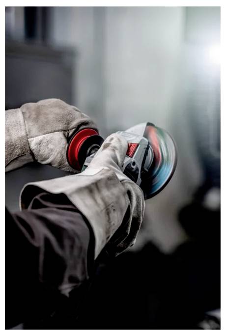 A person wearing protective gloves uses an angle grinder, with sparks and blurred motion indicating active grinding in progress.