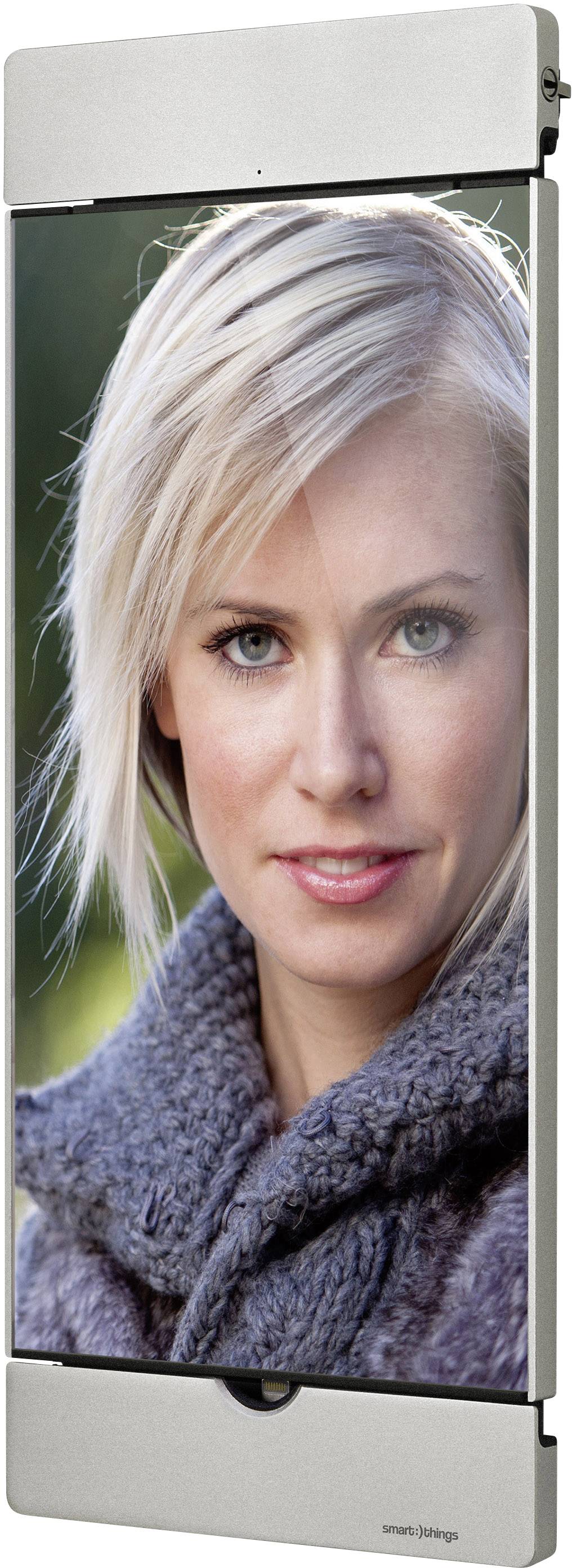 A person with blonde hair is wearing a grey jumper and looking directly at the camera. The background is out of focus.