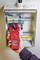 A person is measuring electrical current in an open electrical cabinet using a red clamp meter. The display shows '2.108'.