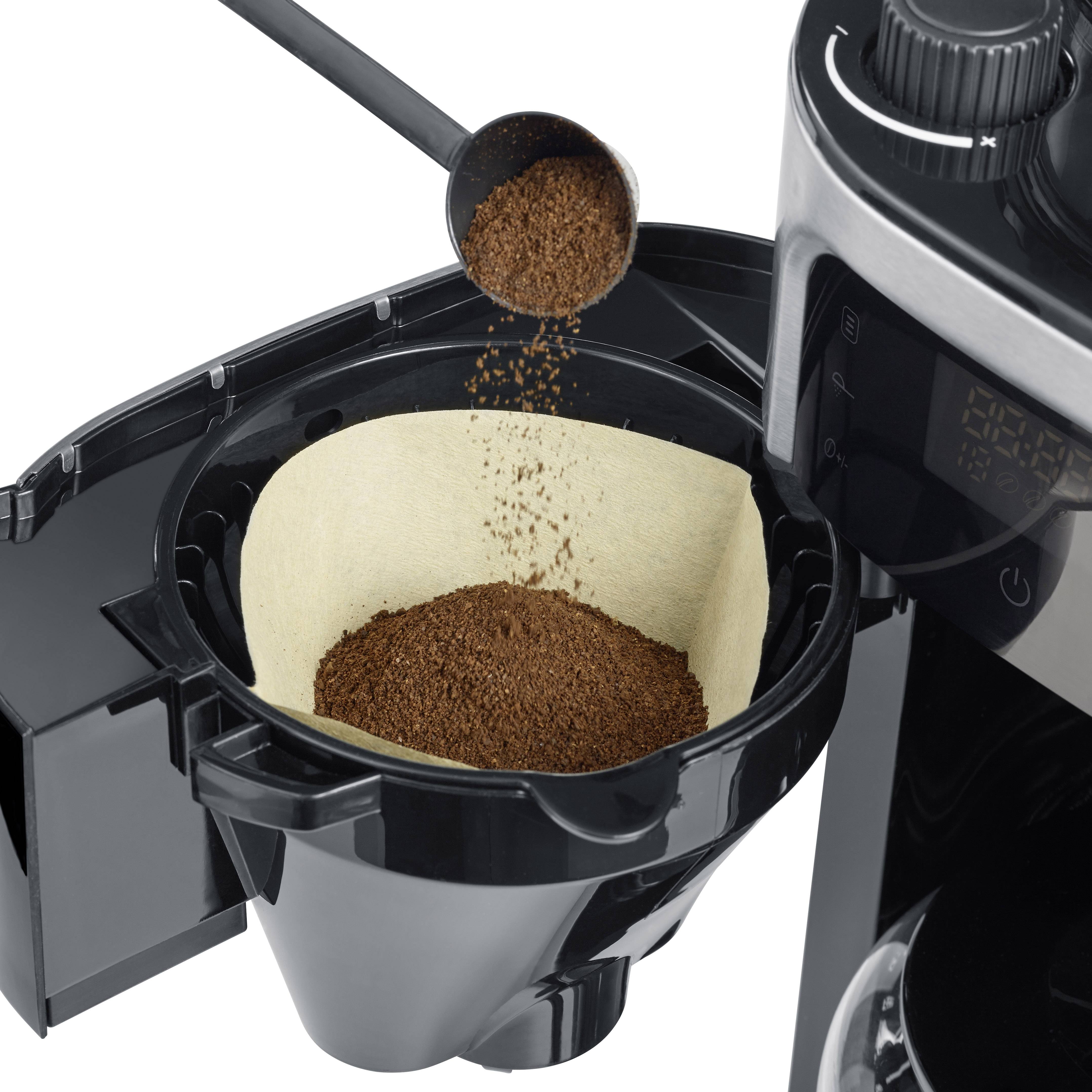 Coffee filter machine with an open filter holder. Ground coffee is being spooned into a paper filter.