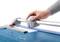 A hand operates a paper cutter and cuts a white sheet of paper on a blue background.