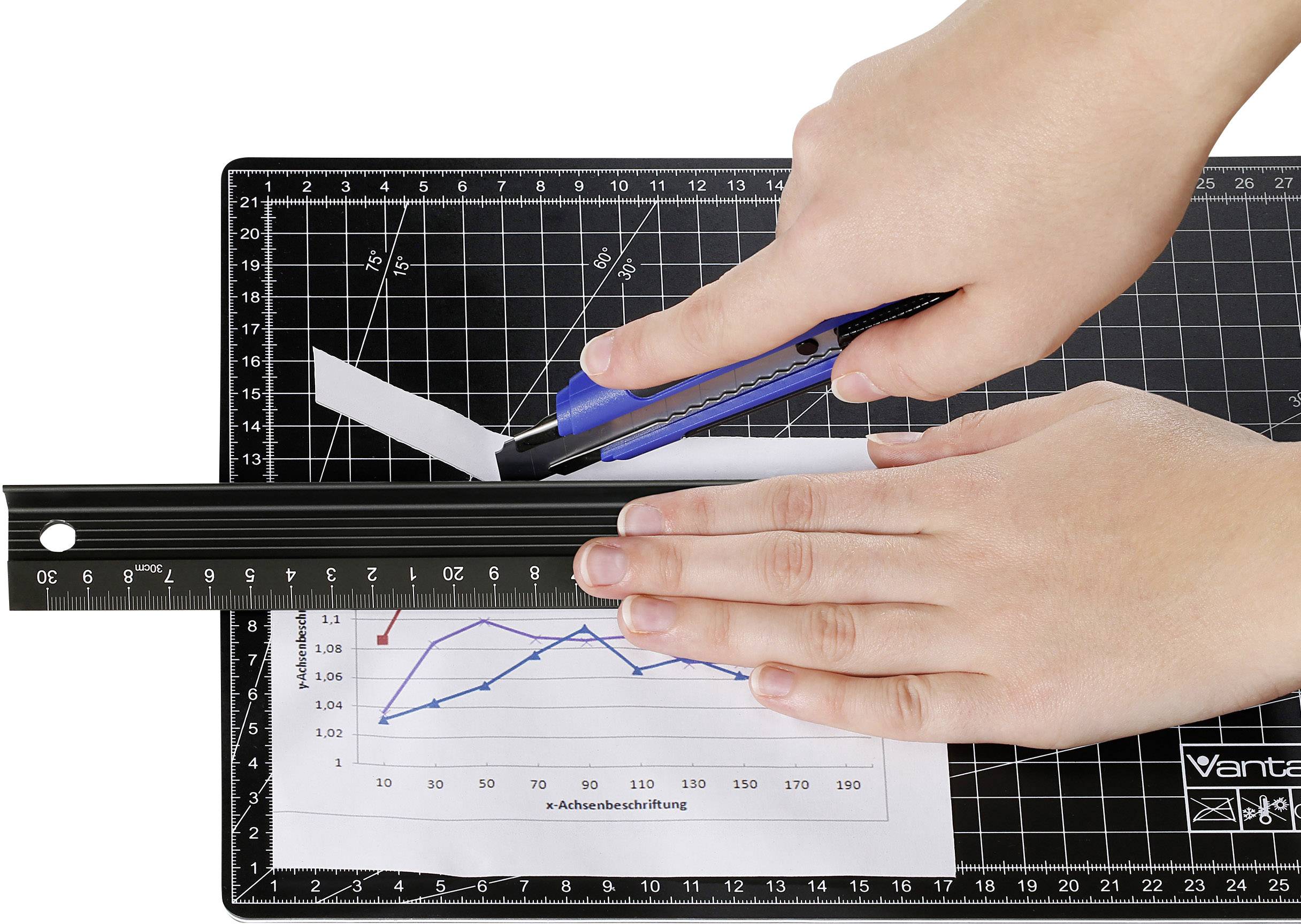 Two hands are using a craft knife and a ruler to cut a document with a line graph on a cutting board.