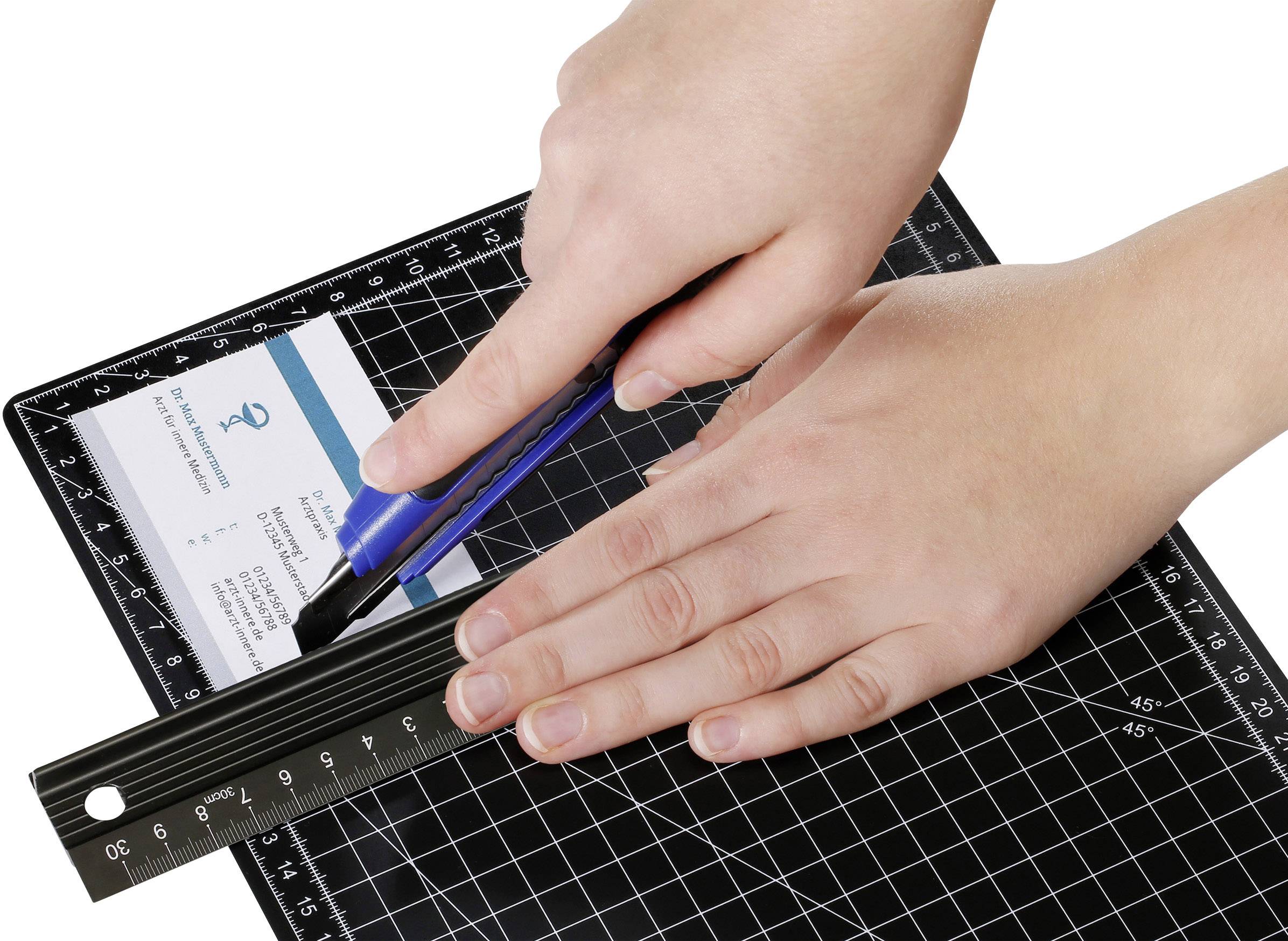 'Hands cutting a business card with a craft knife on a cutting mat along a ruler.'