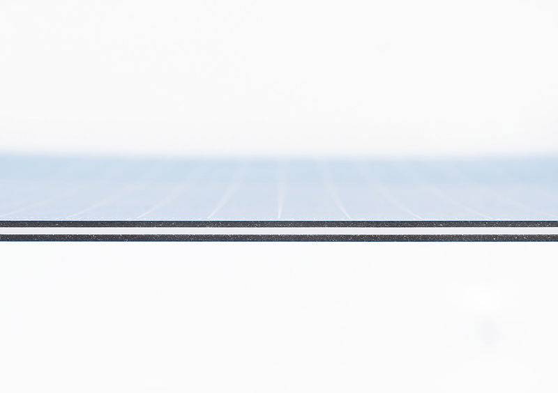 Close-up of a thin edge of a blue solar module against a white background. The lines indicate the solar panel structure.