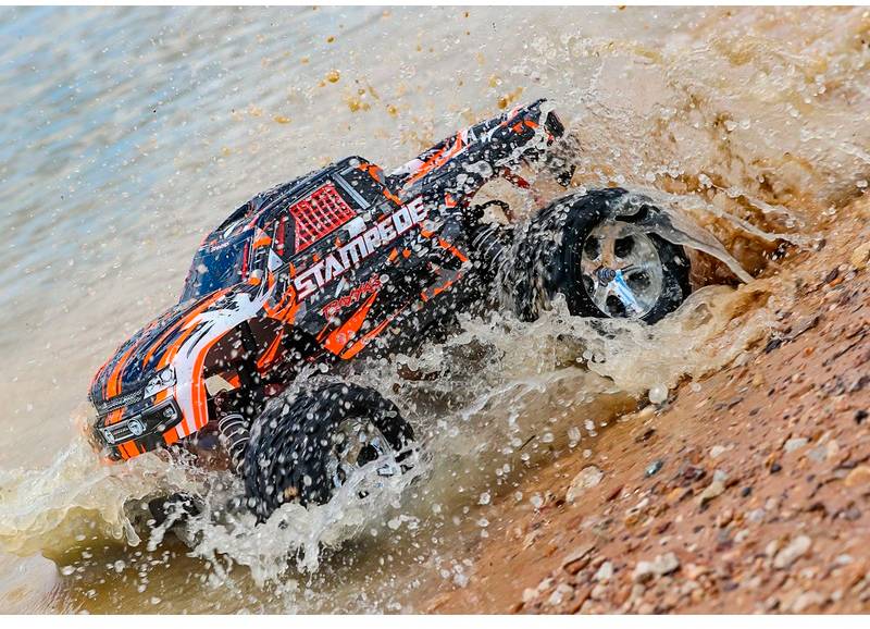 A remote-controlled car drives over wet sand and splashes water as it dynamically moves through a sandy puddle.