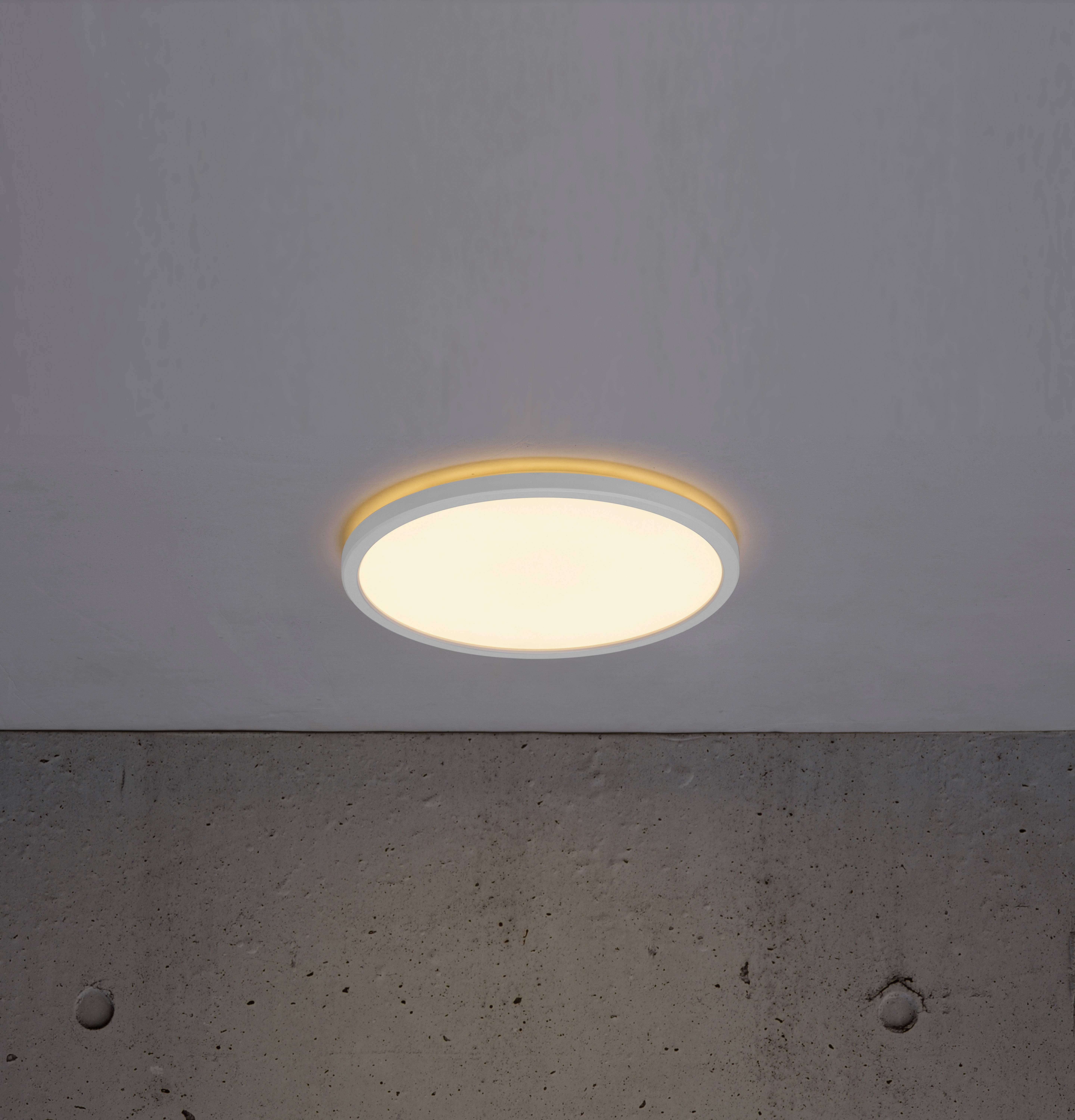 A round ceiling light casts warm light onto a grey, smooth concrete wall.