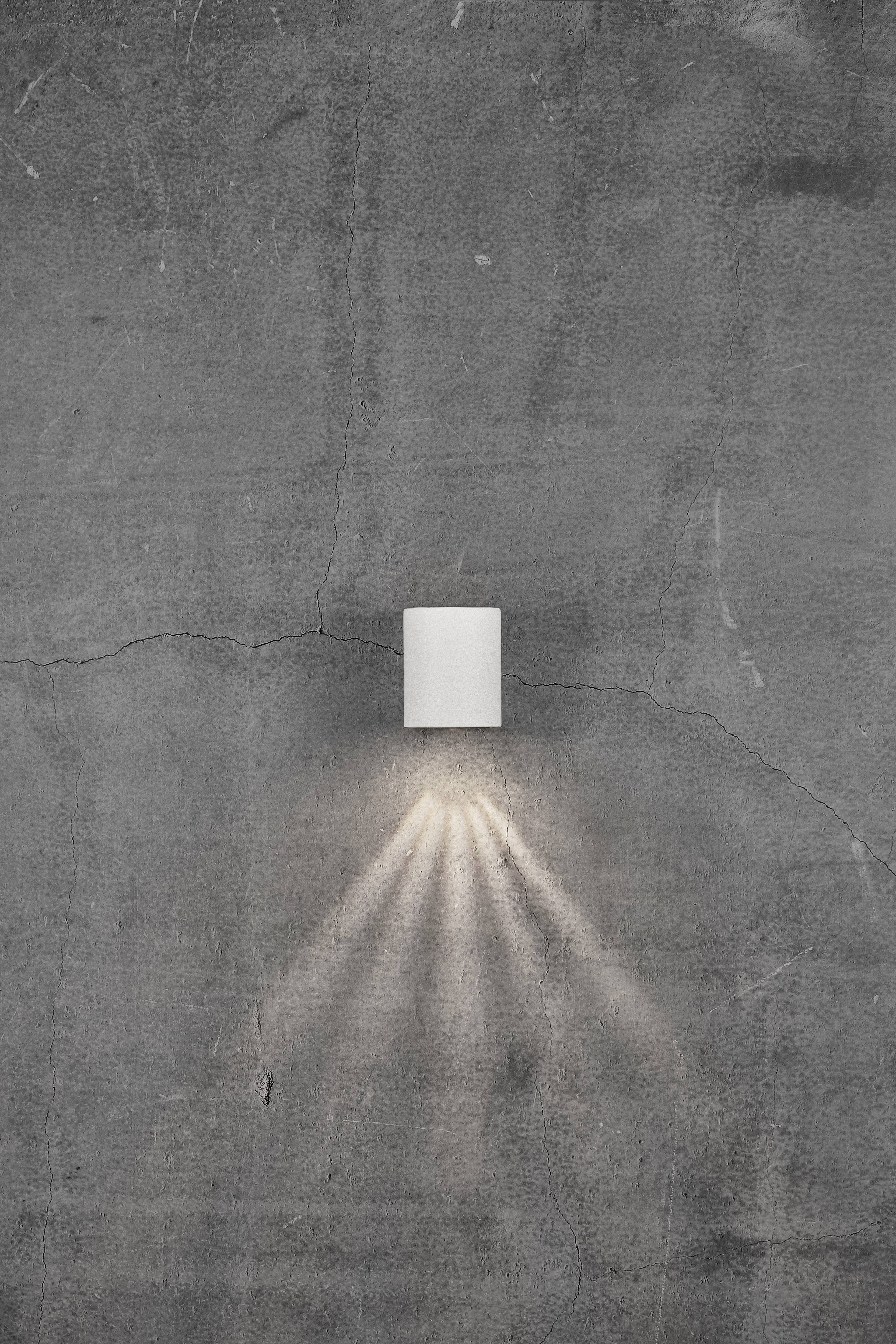 Wall light mounted on a grey, rugged concrete wall, casting light downwards.