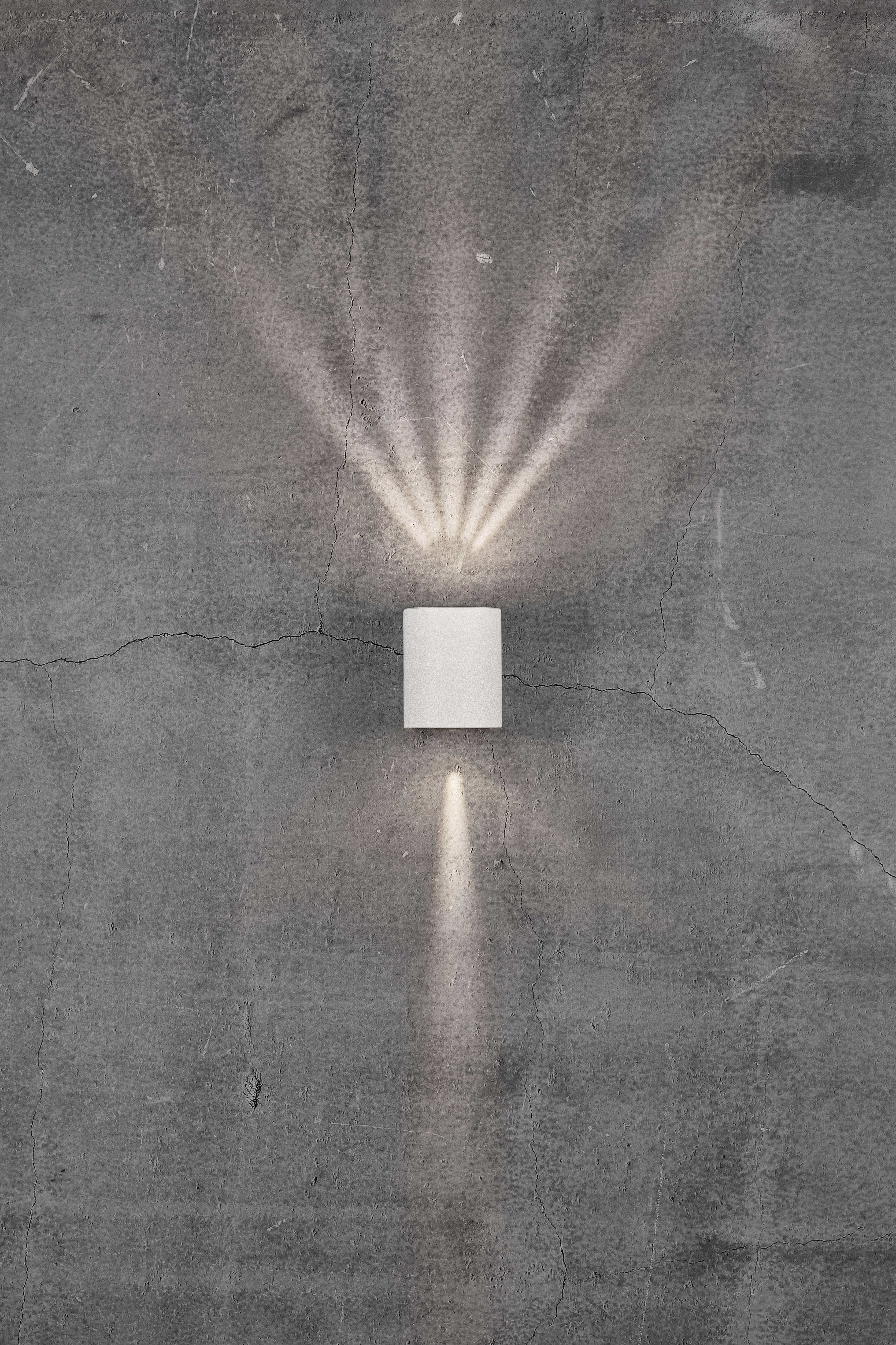 Wall light on a grey concrete wall, casting light rays upwards and downwards, creating a decorative pattern on the wall.