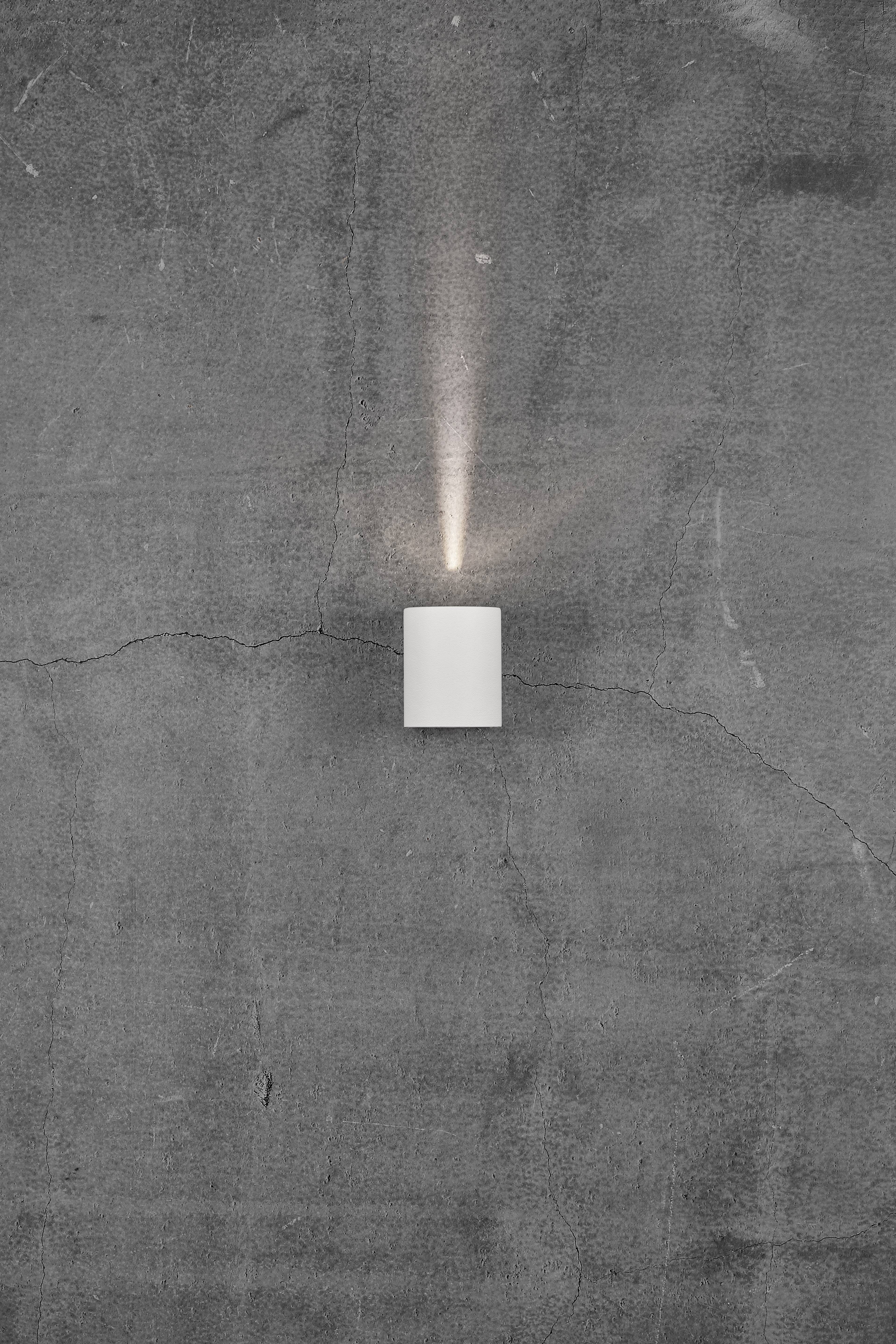 A small, rectangular lamp on a grey, cracked concrete wall. The lamp emits a faint light upwards.