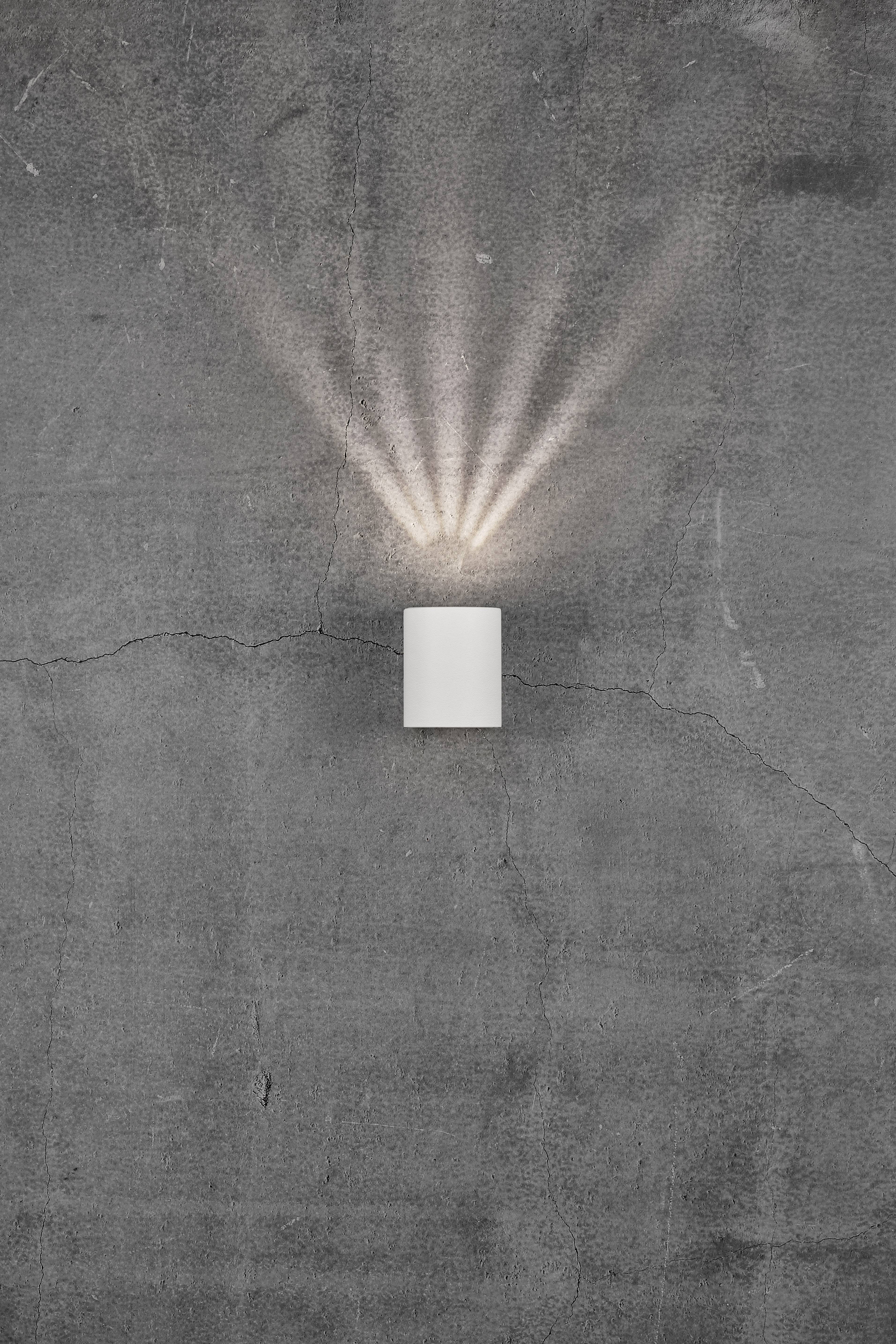 A white wall light on a grey, cracked concrete wall, projecting light rays upwards and downwards.