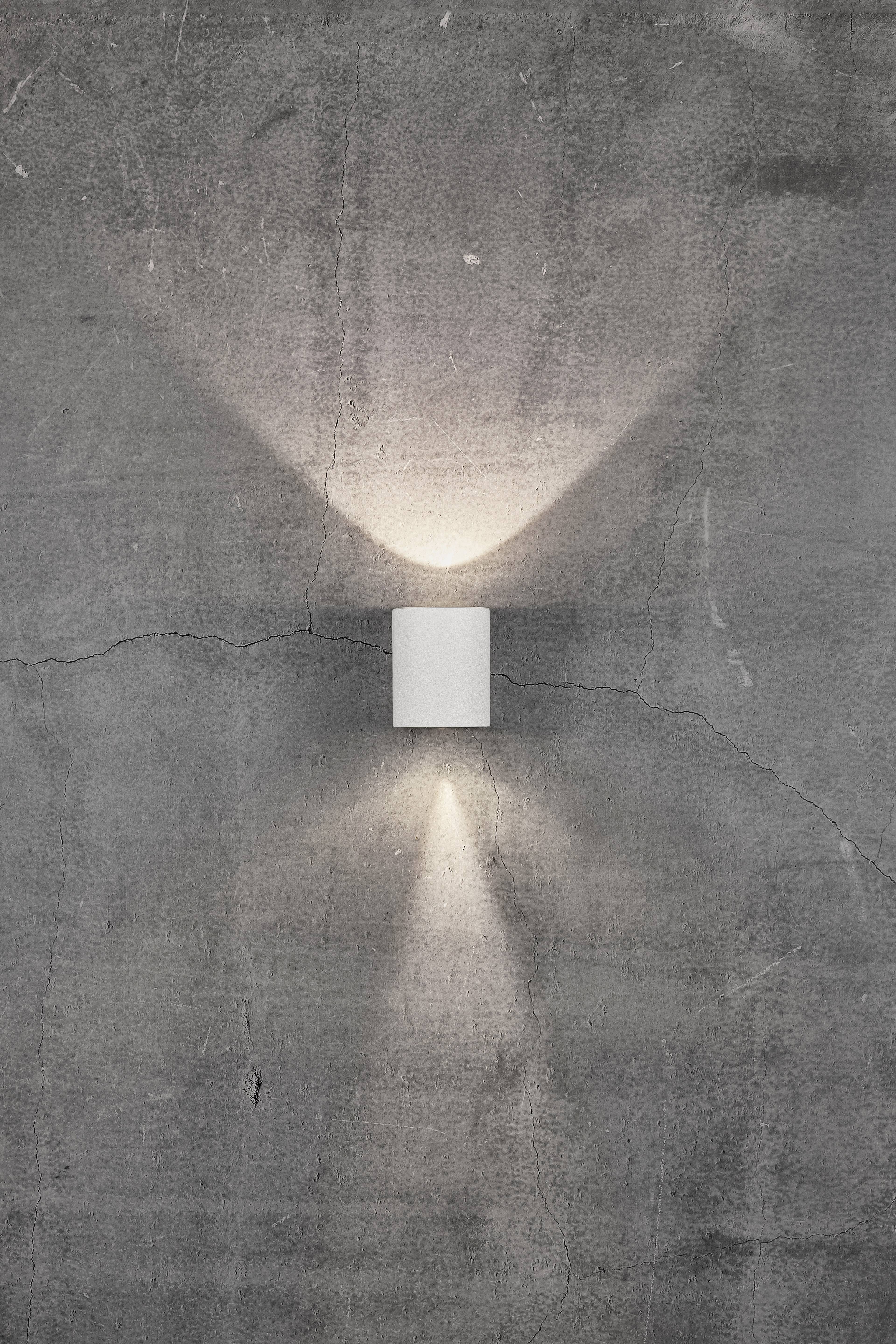 Wall light on a concrete wall, casting light upwards and downwards, creating V- and A-shaped light patterns.