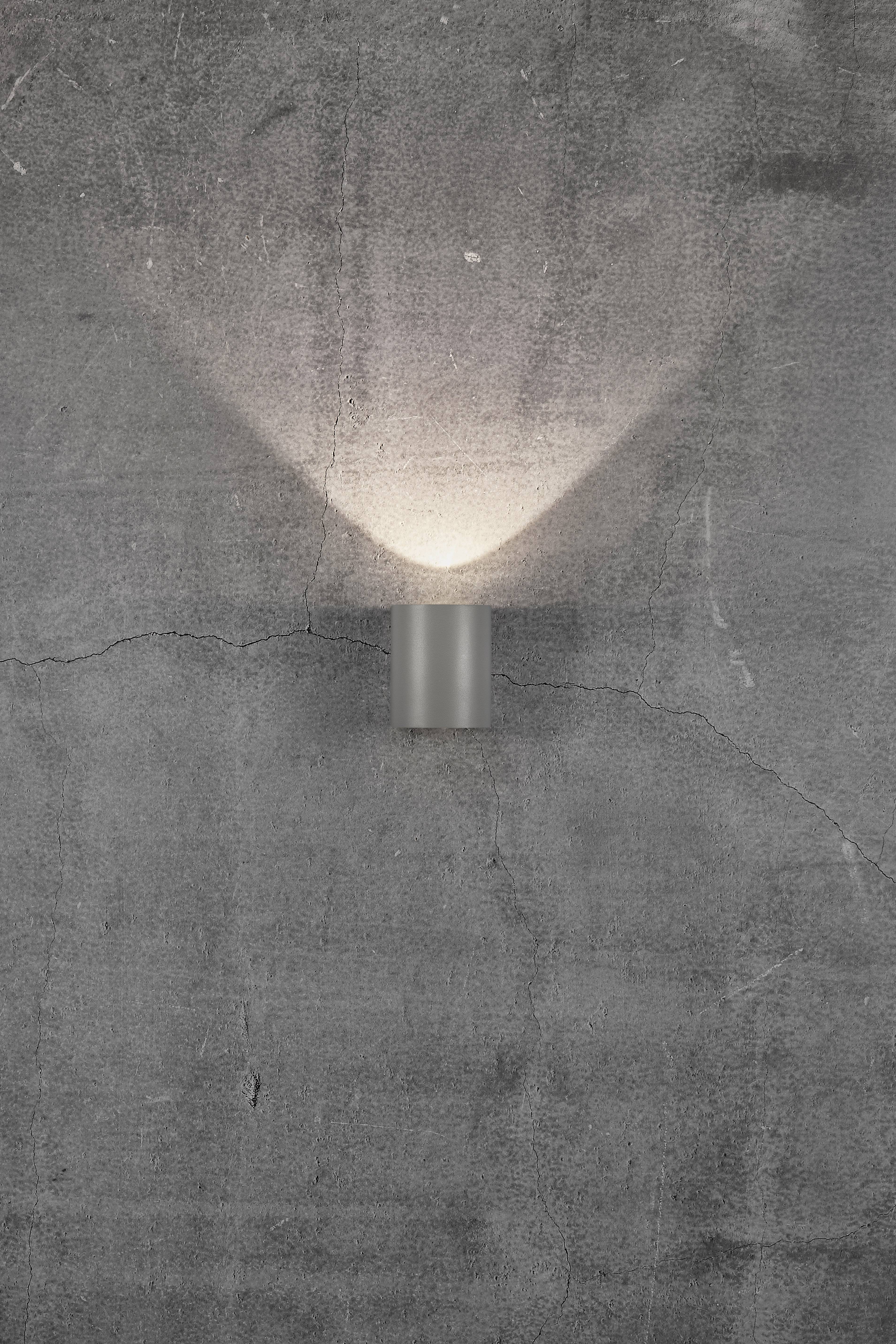 Wall light on a grey concrete wall, casting warm, diffused light upwards and downwards, creating a calm and atmospheric ambience.