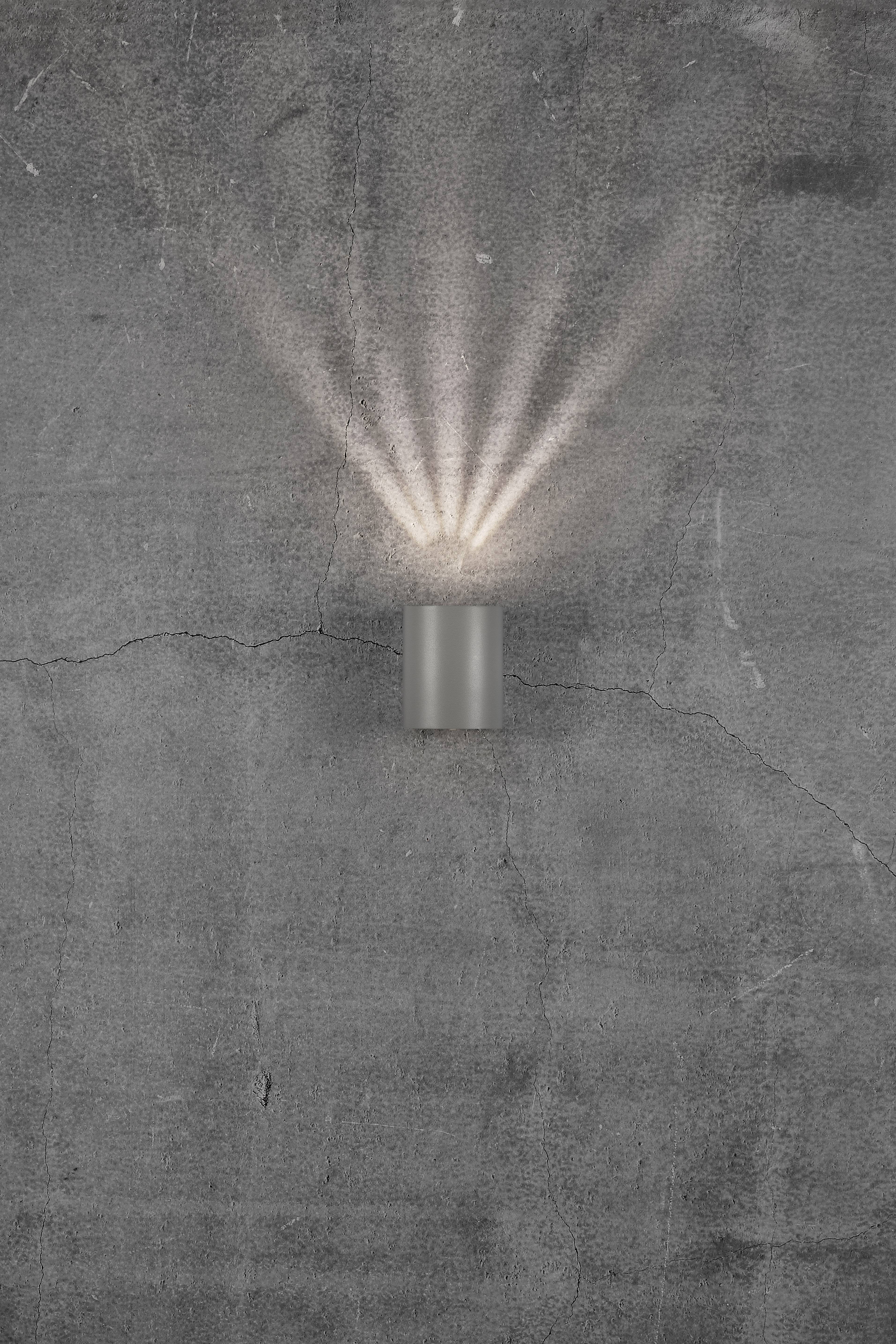 Wall light on a grey wall shines upwards and downwards, creating decorative light effects.