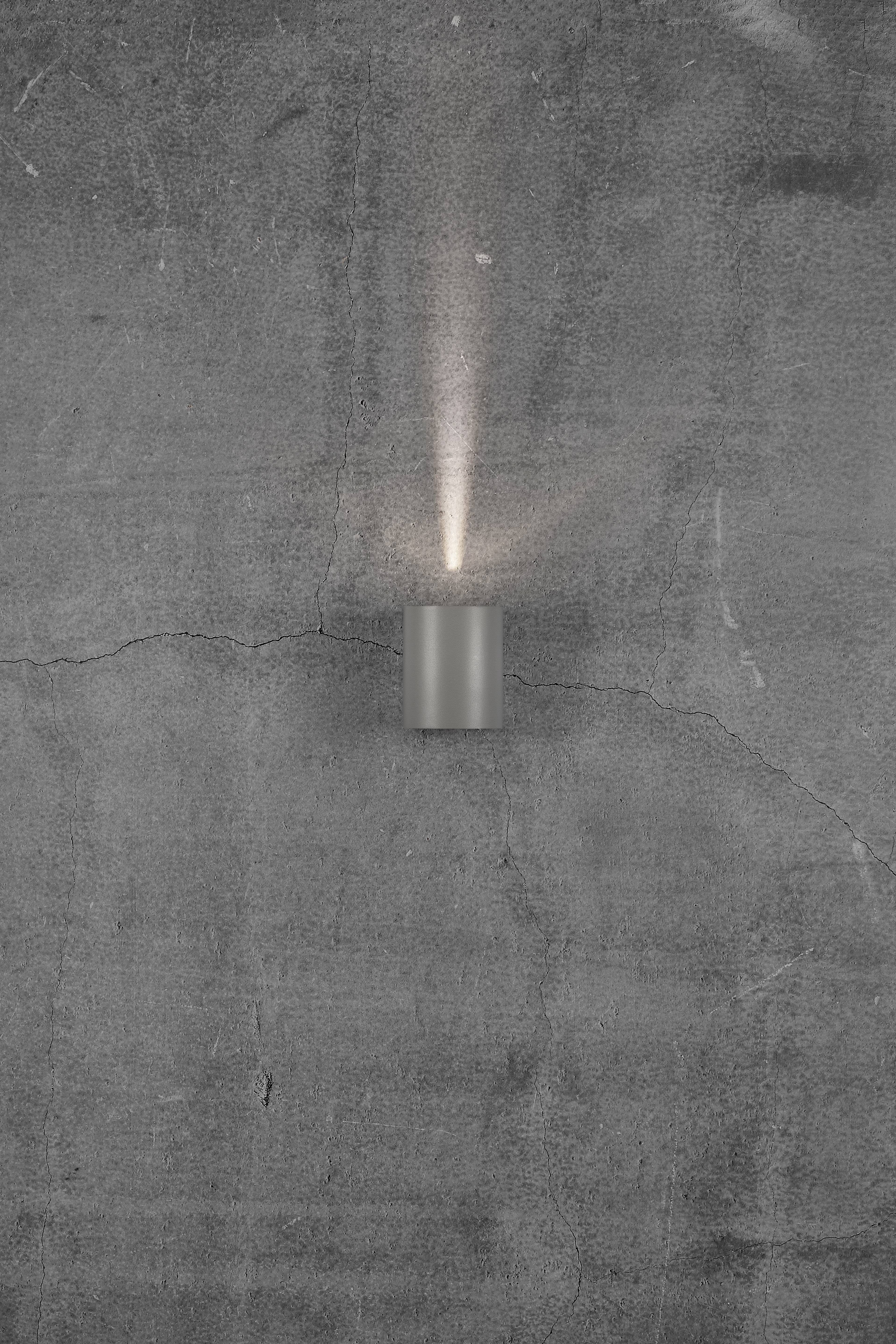 Grey wall with a crack, with a small, round wall light attached that emits soft, upward-facing light.