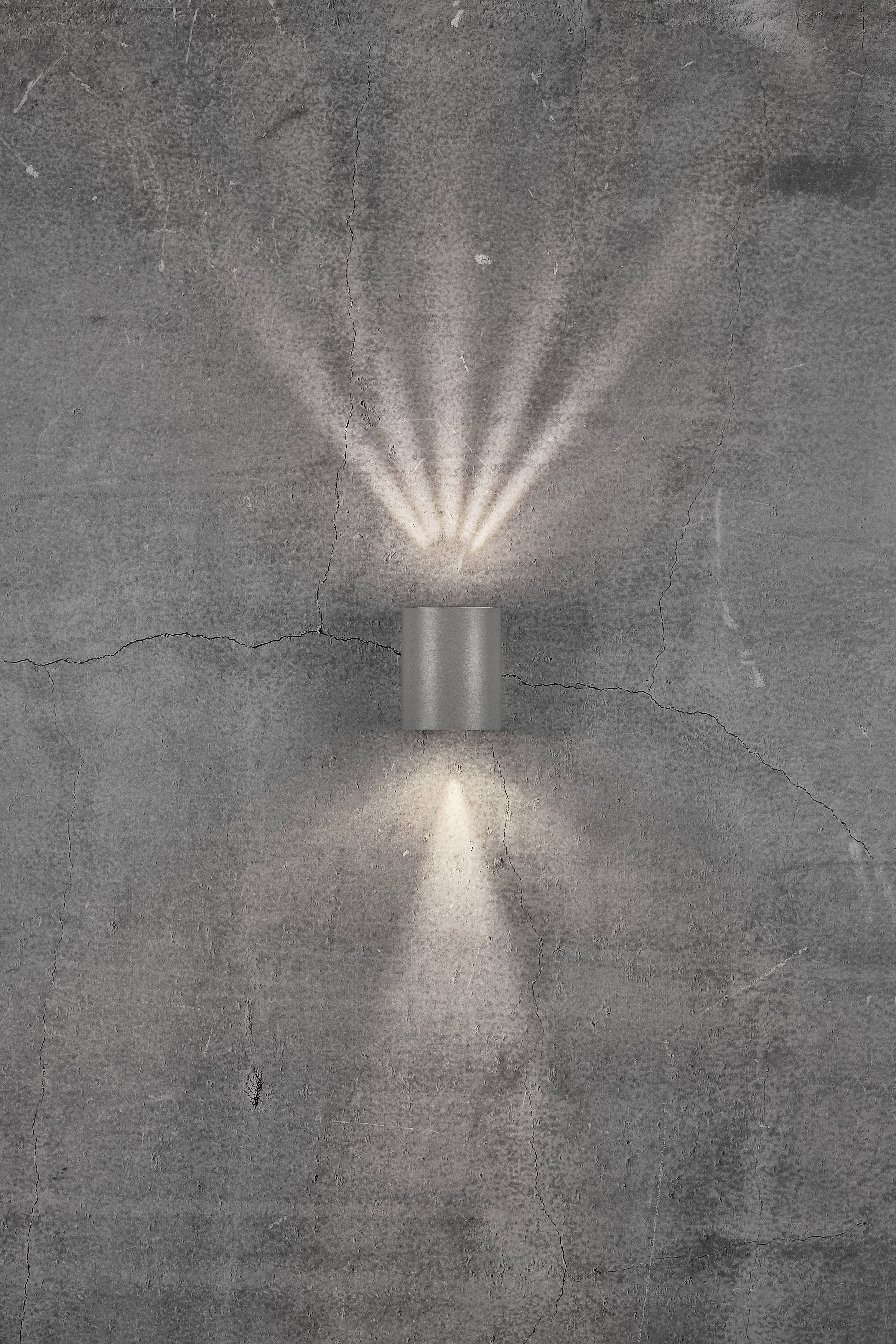A wall light casts a diffused light pattern upwards and downwards onto a grey, cracked concrete wall.