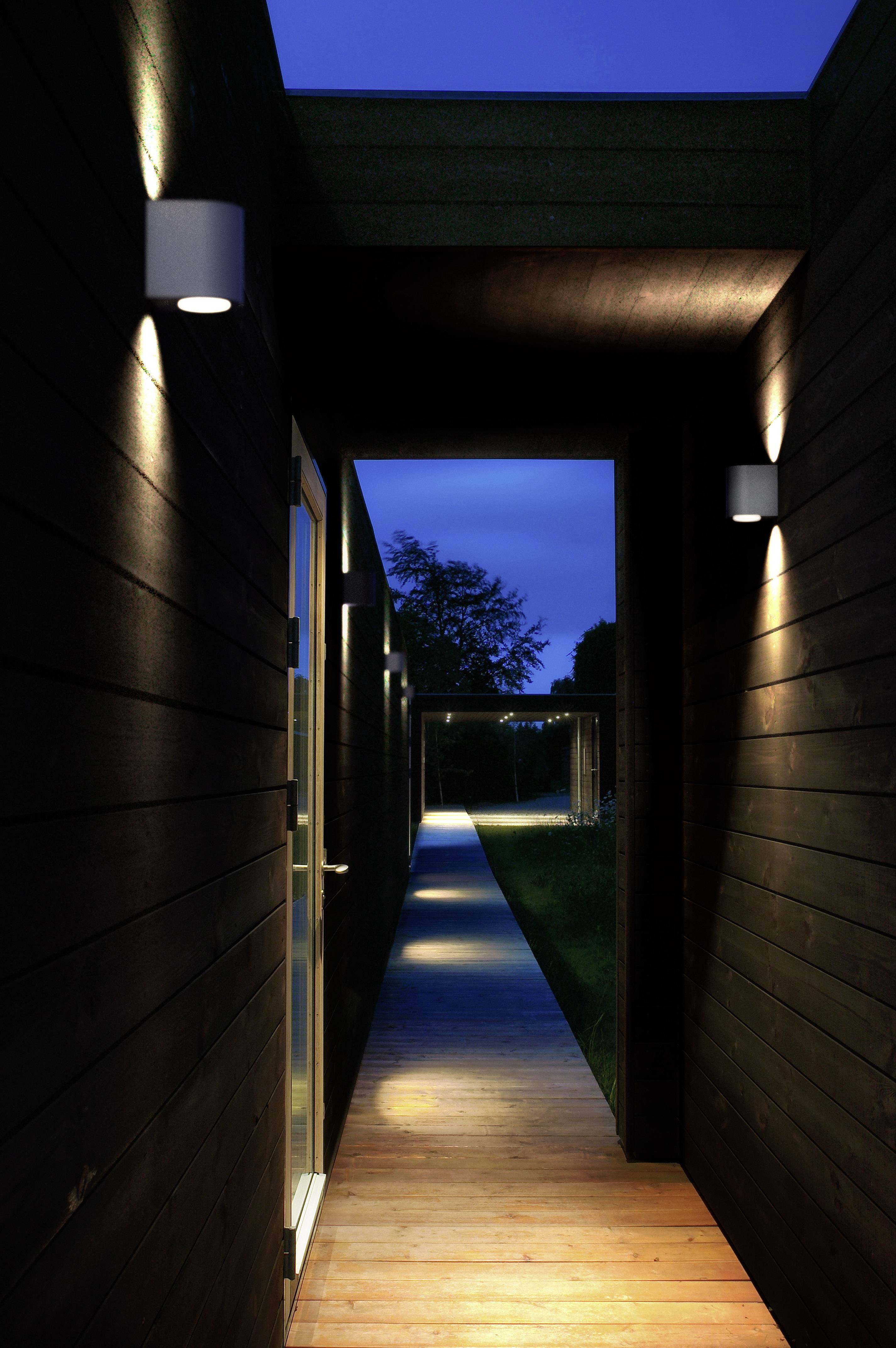 A narrow, illuminated wooden walkway leads through a covered corridor of dark wood. Exterior lighting and twilight.