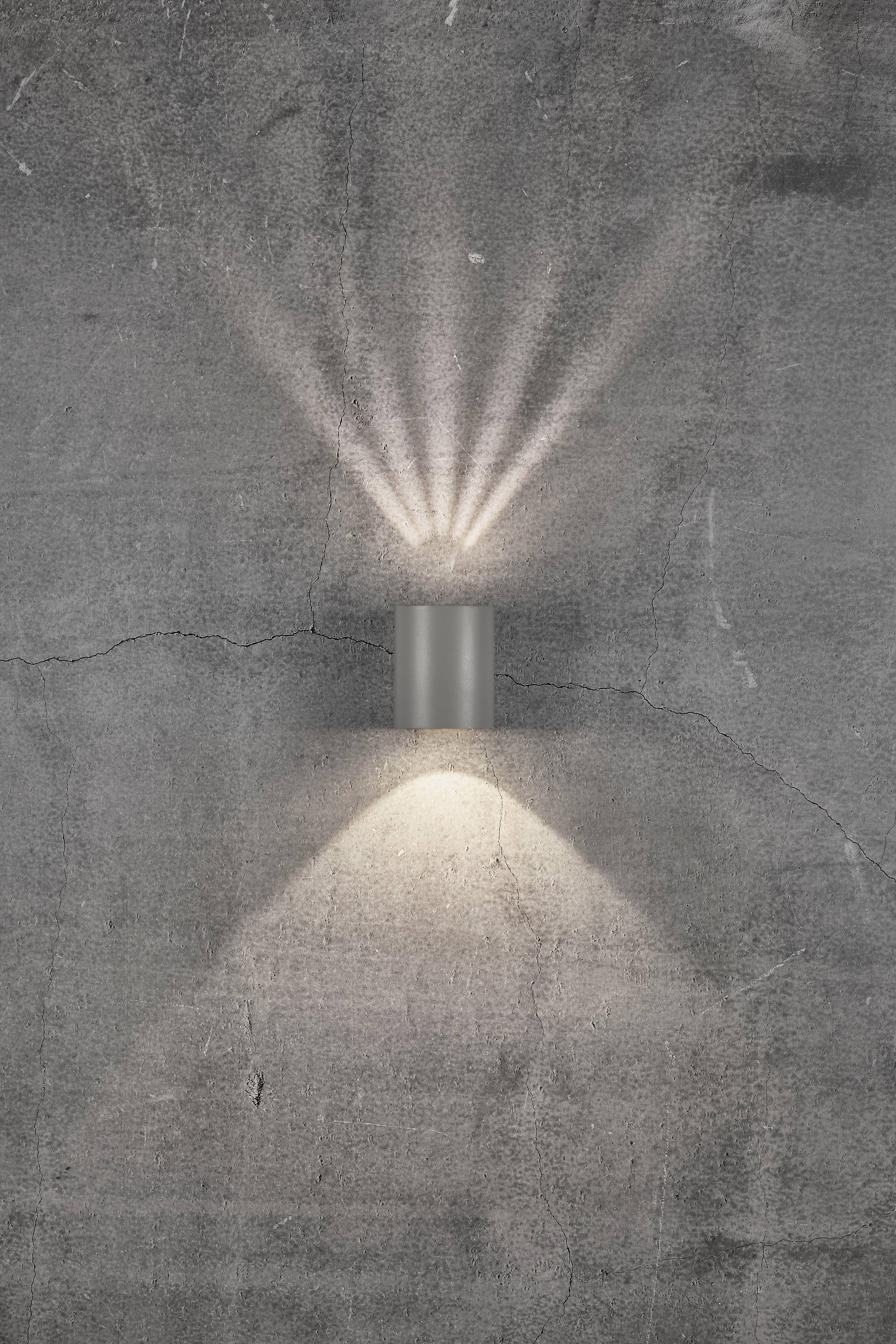 Wall light on a grey concrete wall, casting light upwards and downwards, creating a decorative pattern.