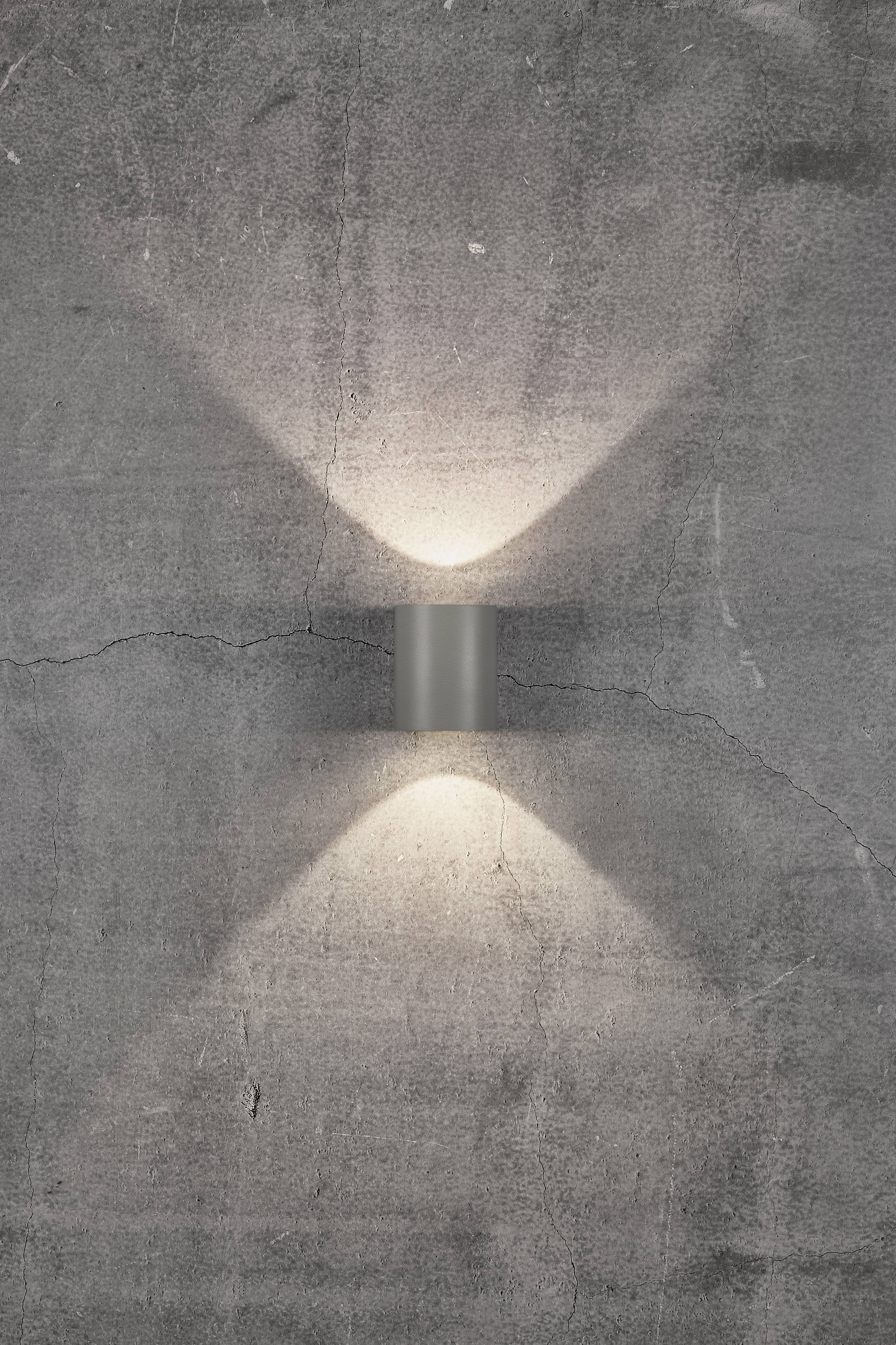 Wall light on a grey, cracked concrete wall, casting light upwards and downwards and creating an X-shaped pattern.