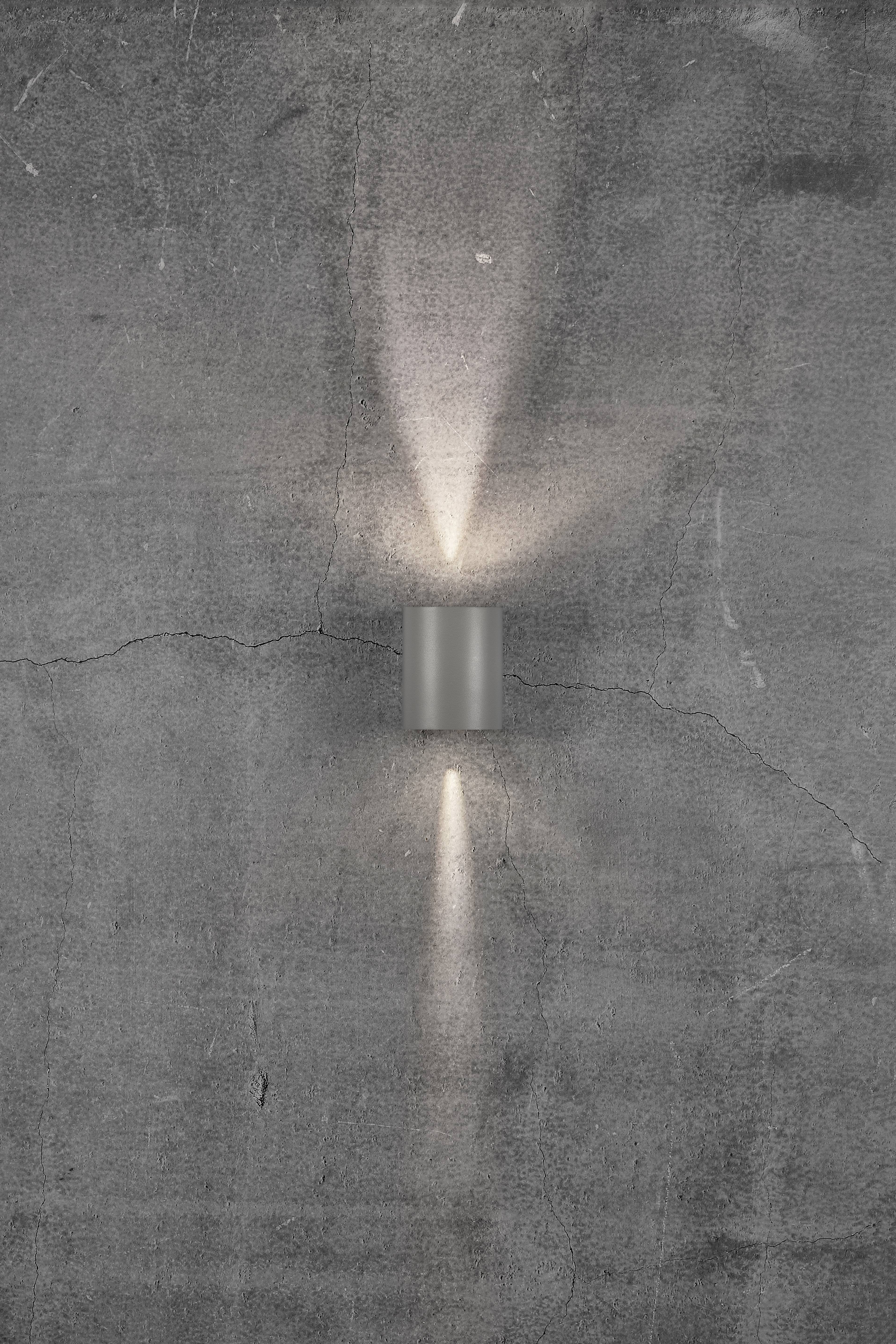 Wall light on a grey, textured surface, emitting light rays upwards and downwards. Modern and minimalist design.