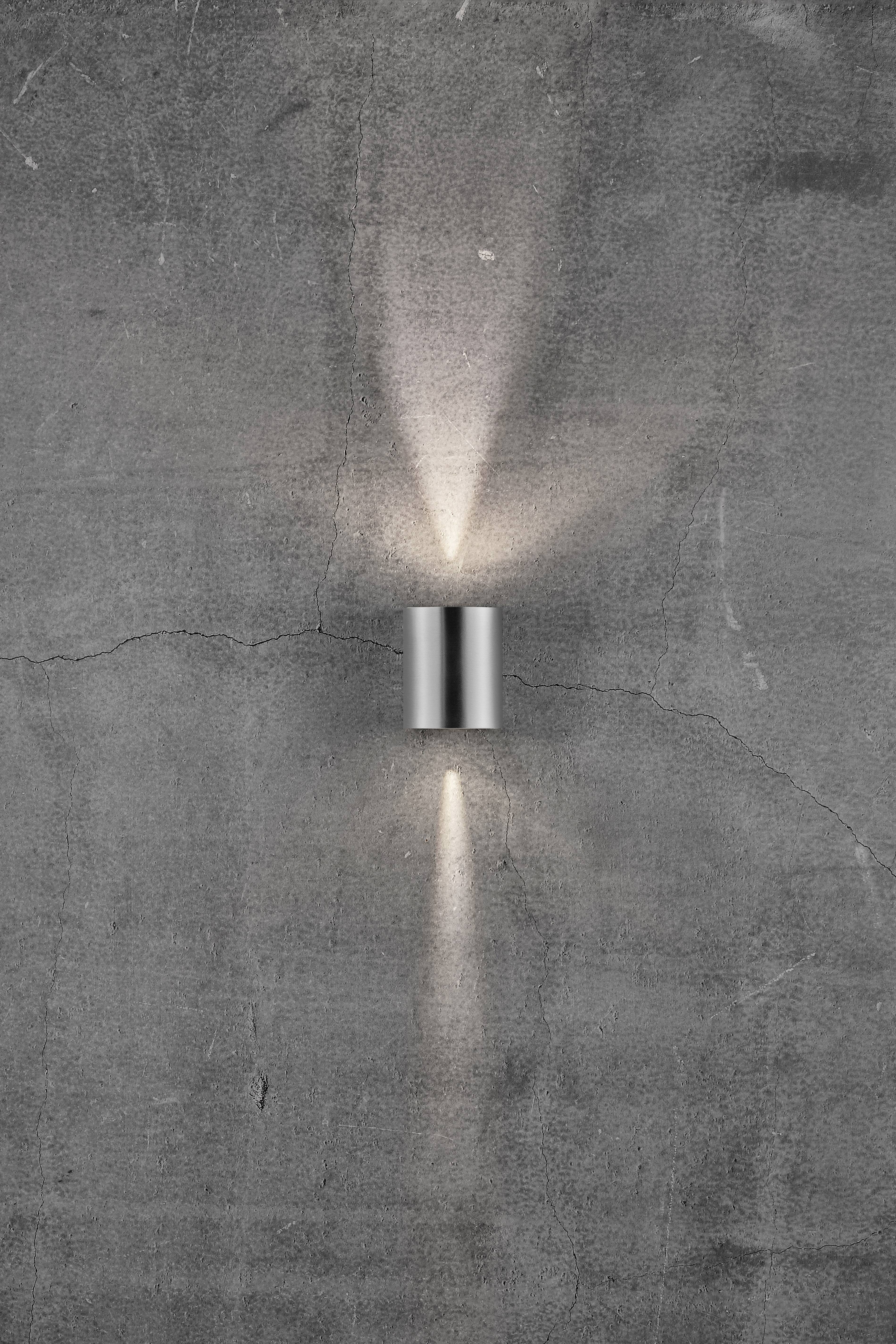 Wall light mounted in front of a grey, cracked concrete wall, casting light rays upwards and downwards. Modern, sleek design.