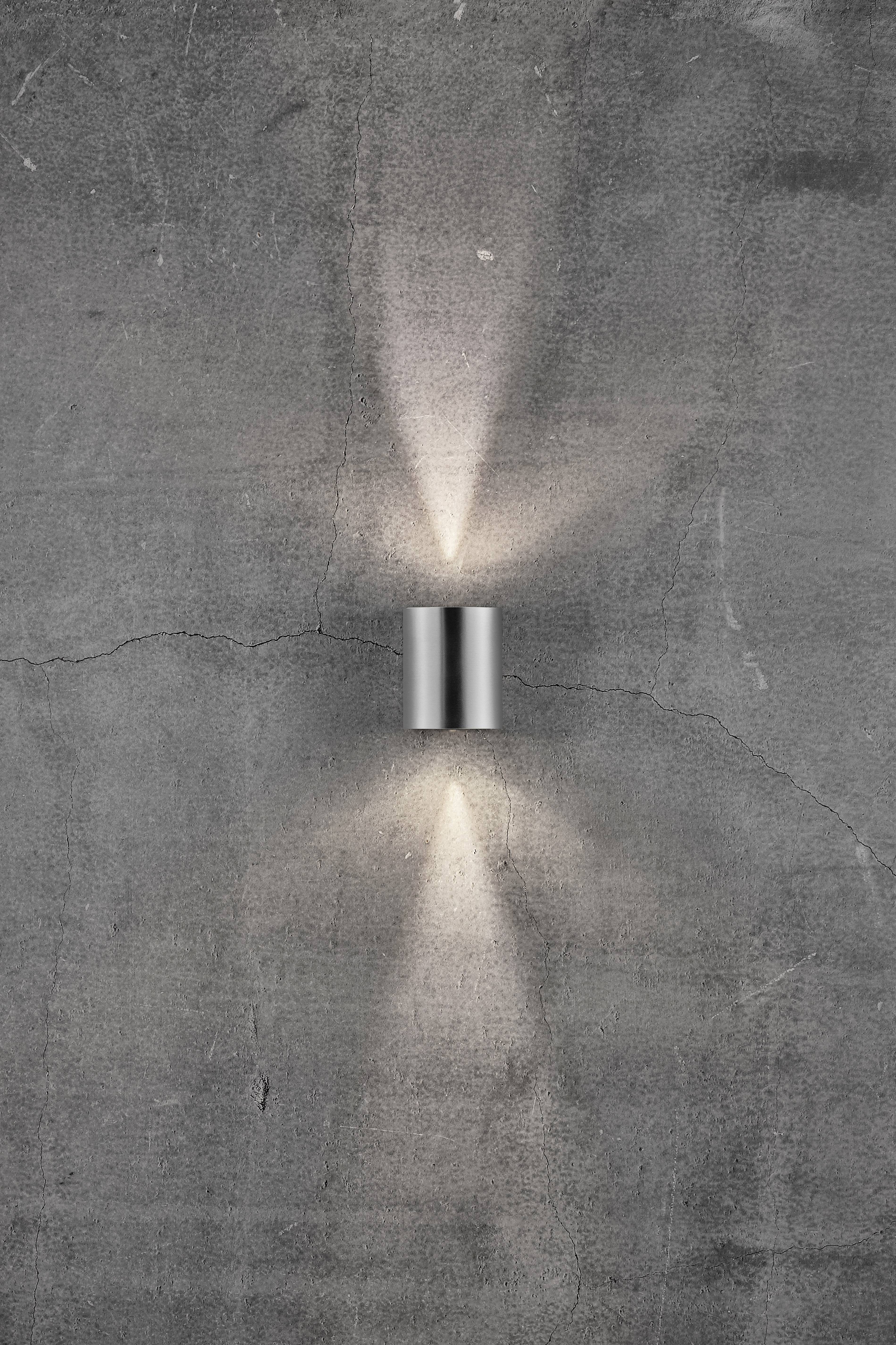 Wall light mounted on a rough concrete wall, casting light upwards and downwards, shadow play on the wall creates a modern atmosphere.