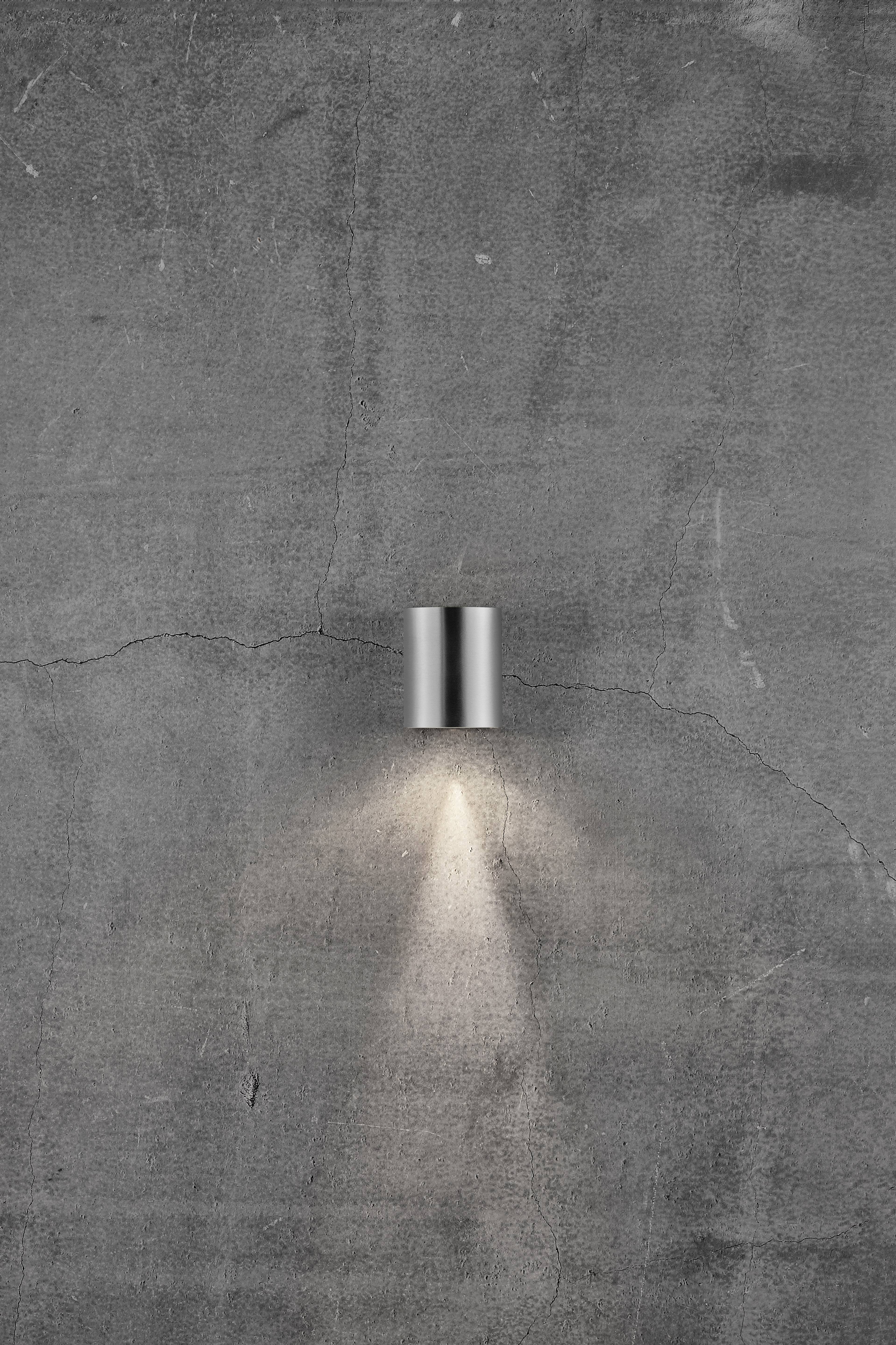 A simple, modern wall light on a rough, grey concrete wall, casting downward light onto the surface.