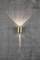 Wall light made of brass on a grey, textured wall. The light radiates upwards and downwards, creating accents on the wall.