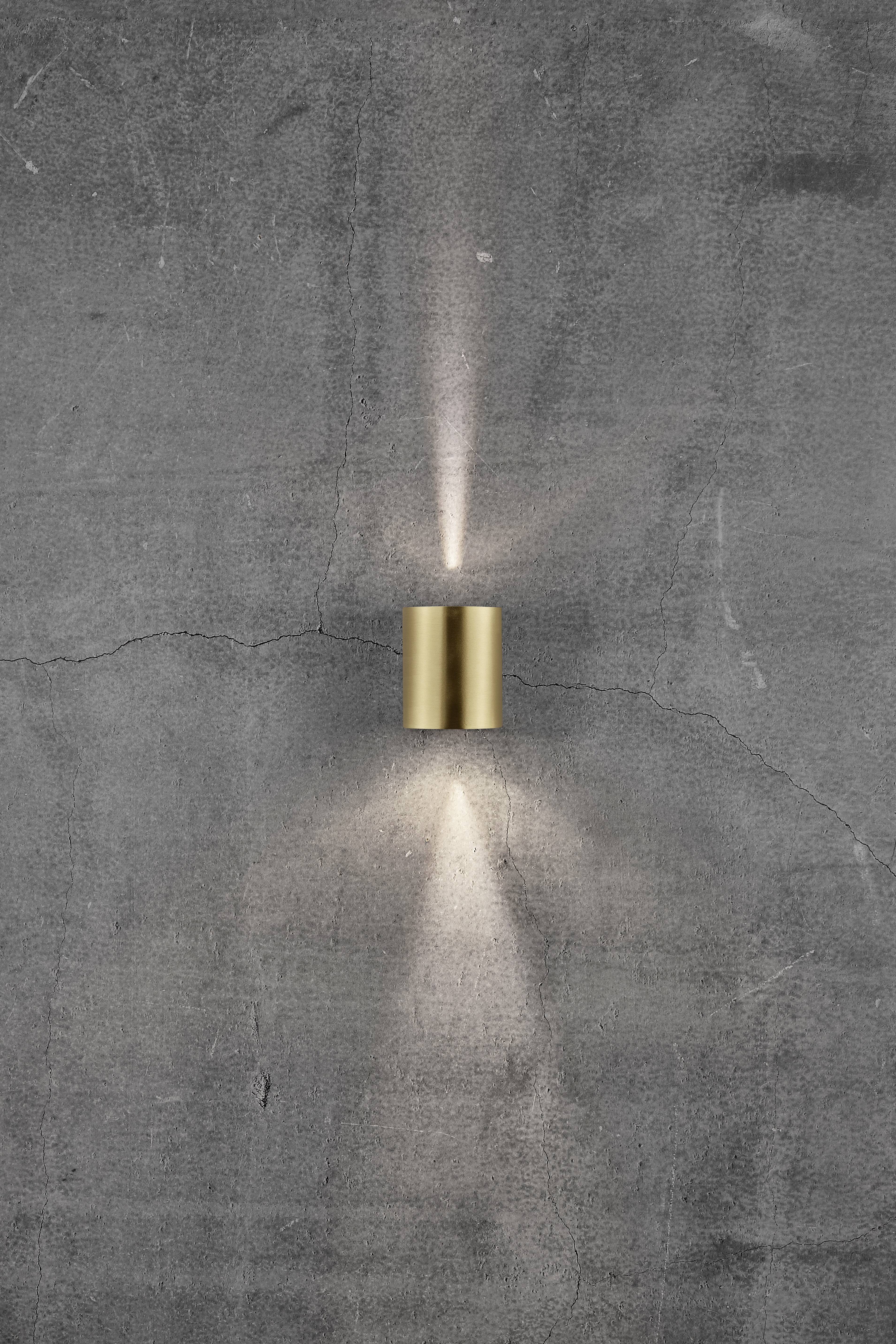 A golden wall light on a concrete wall radiates light upwards and downwards, creating symmetrical light cones.