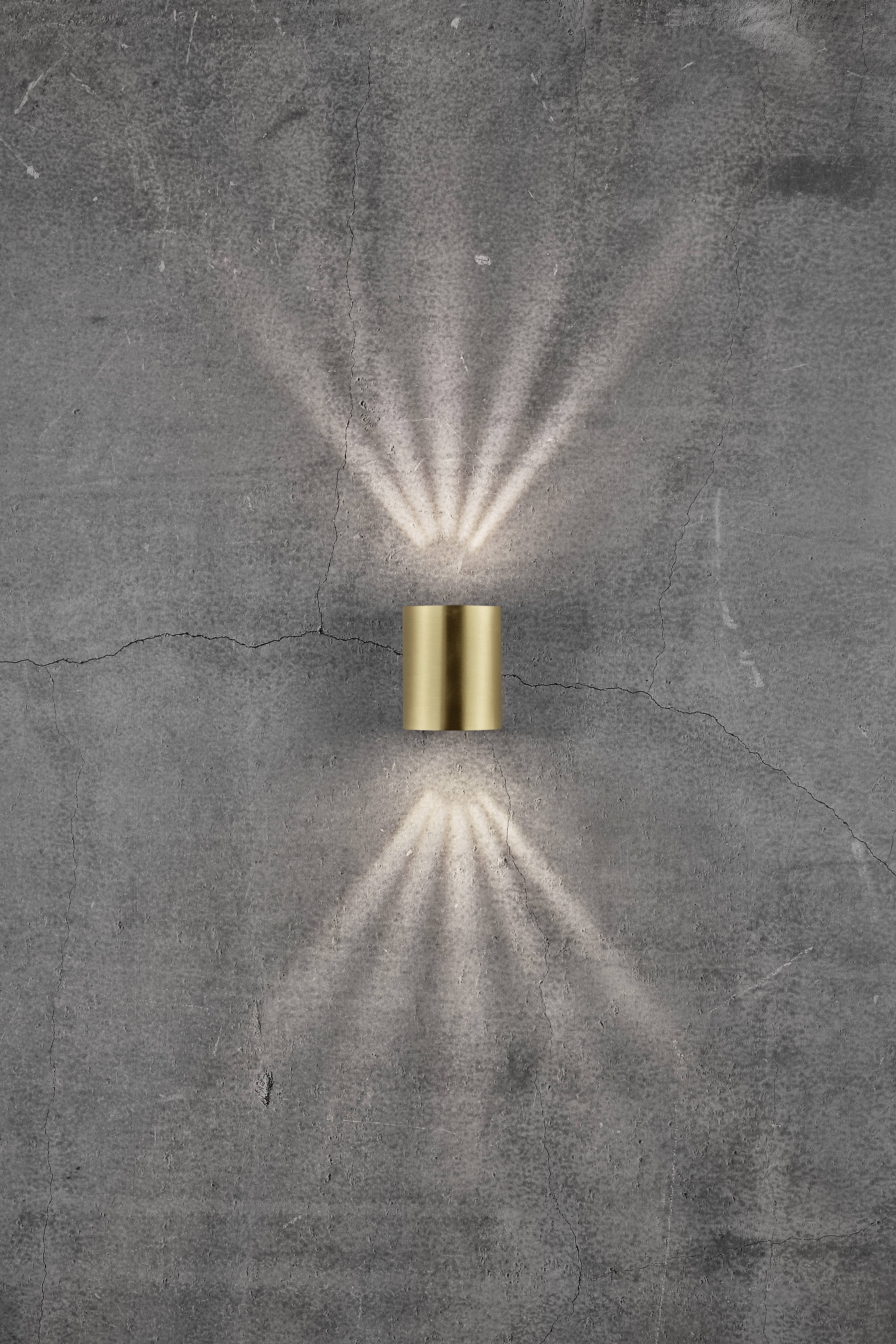 Wall light made of metal on a grey concrete wall, projecting light rays upwards and downwards, creating a decorative pattern.