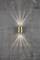 Wall light made of metal on a grey concrete wall, projecting light rays upwards and downwards, creating a decorative pattern.