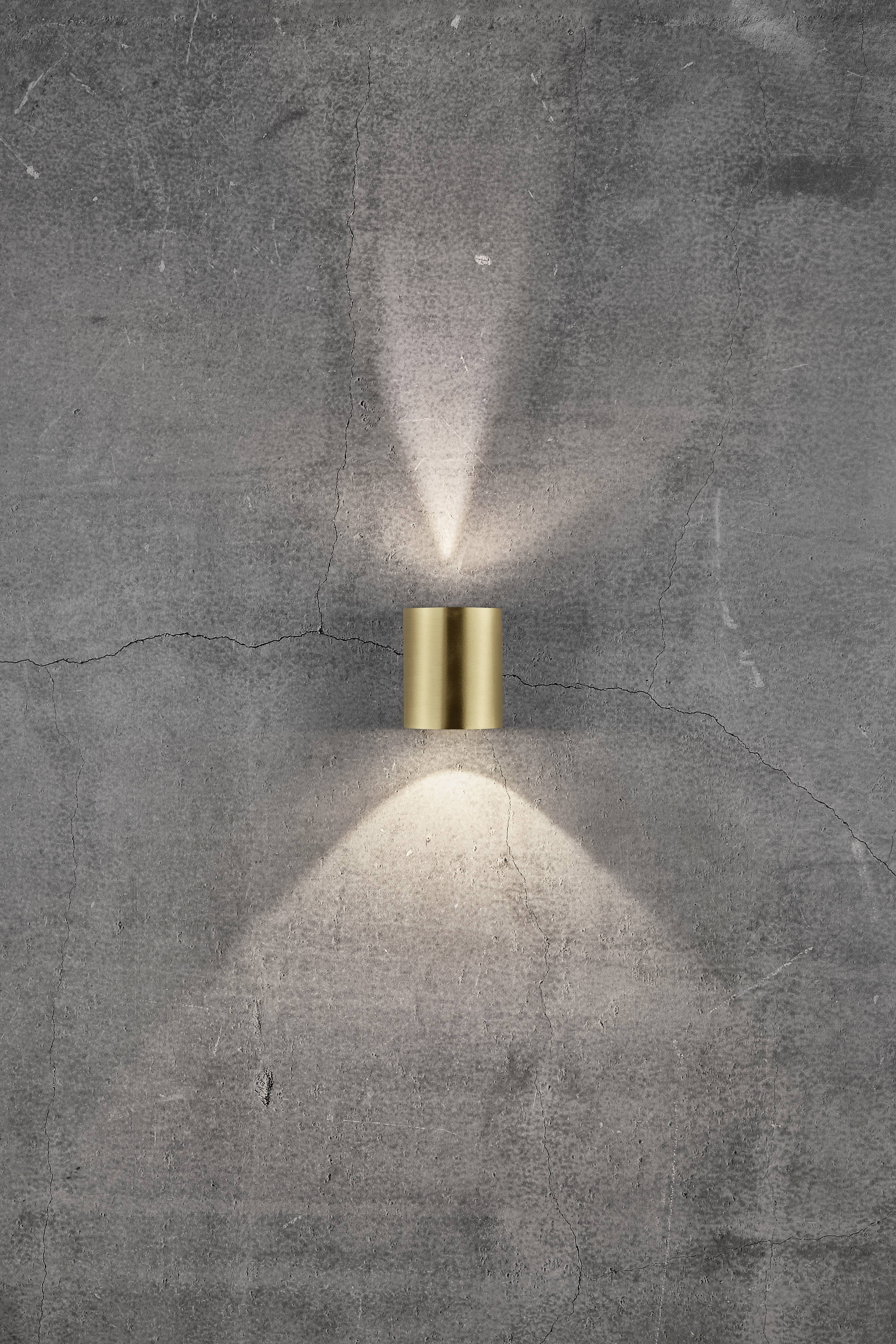 Golden wall lamp on concrete wall, radiating light upwards and downwards, creating a warm light pattern.