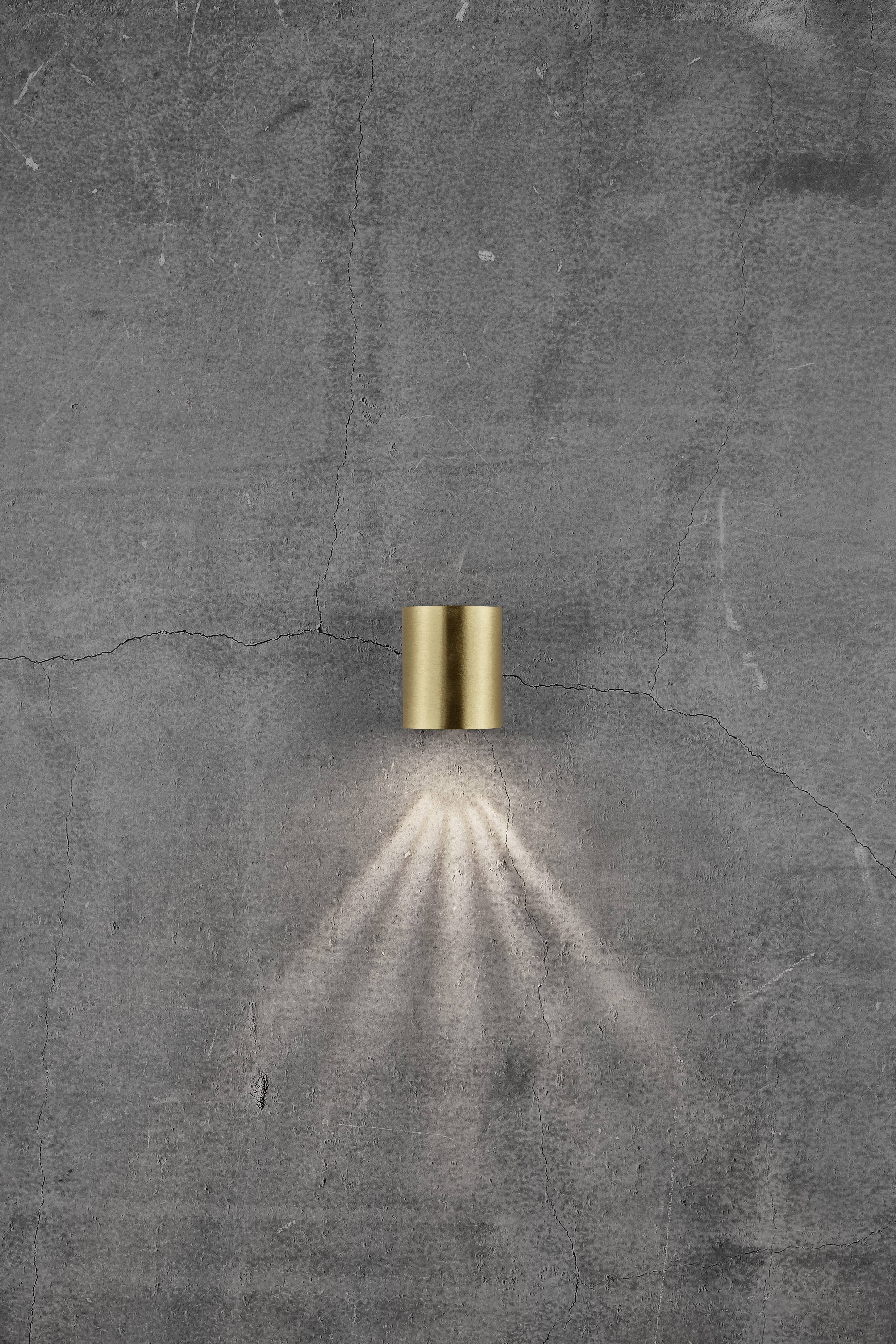 Golden wall light on a grey, textured wall. Light radiates downwards and creates a fan-shaped shadow effect.
