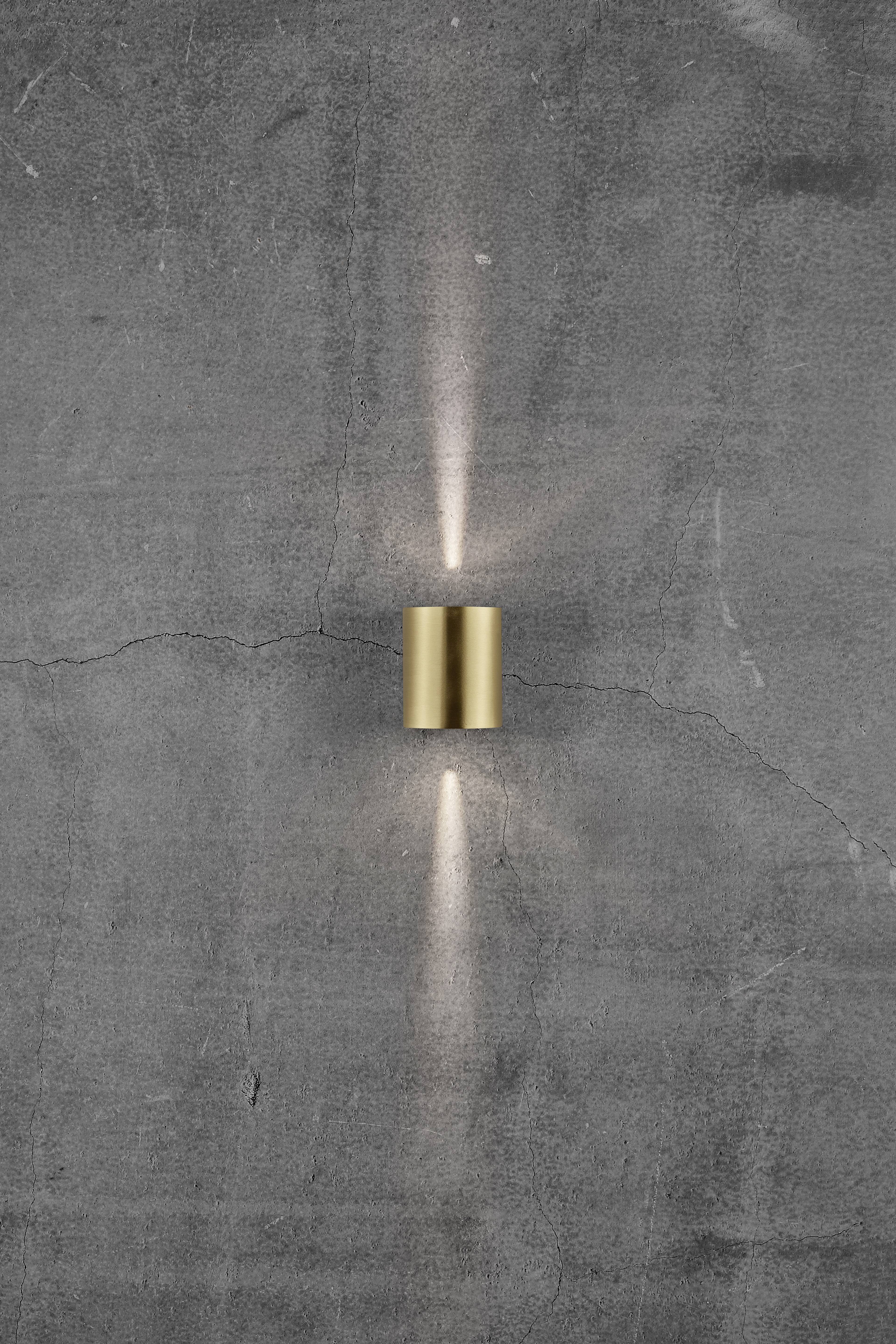A golden wall light on a grey concrete wall radiates soft light upwards and downwards, creating a stylish atmosphere.