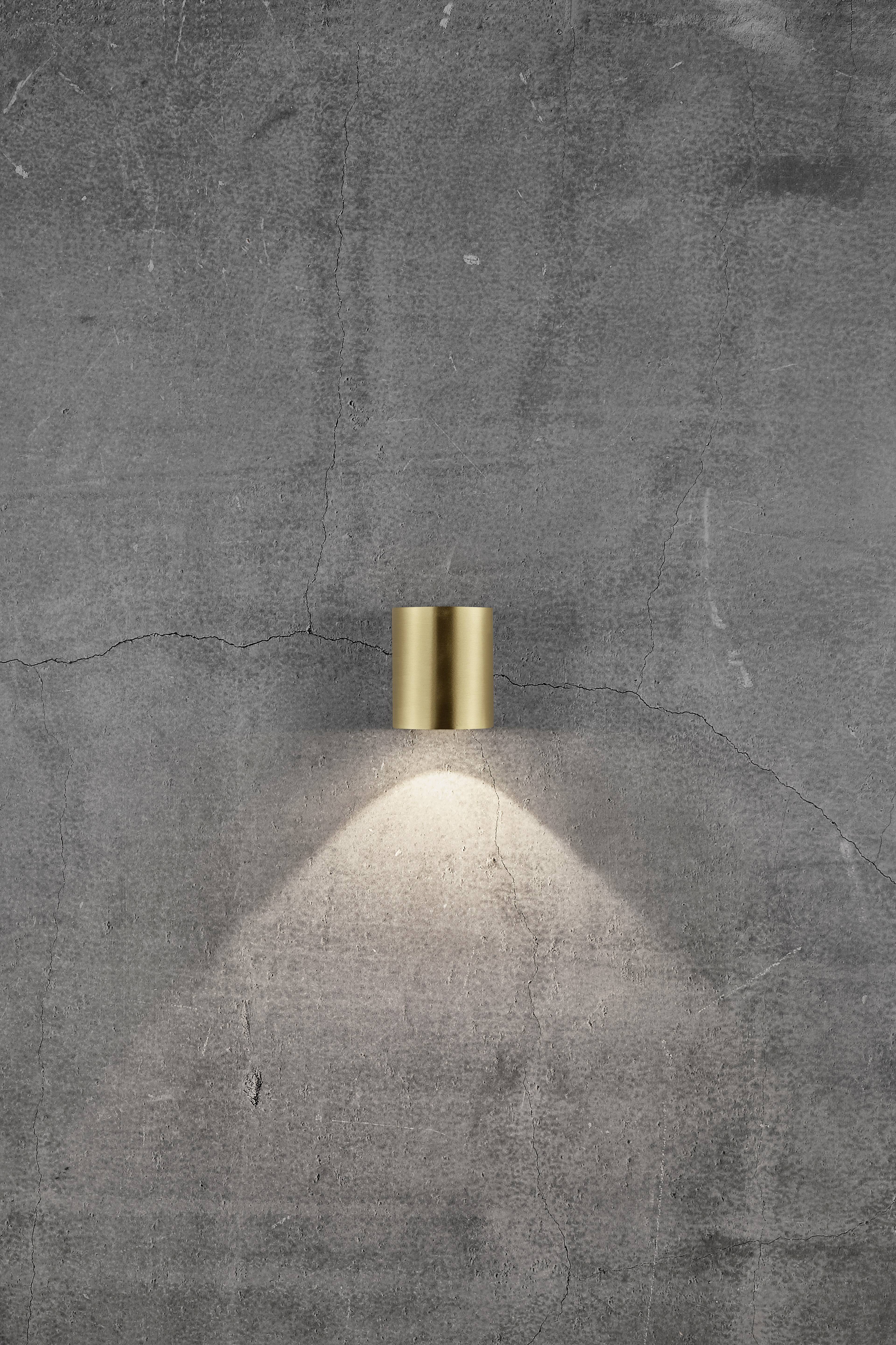 A golden wall light casts light on a grey, textured wall.