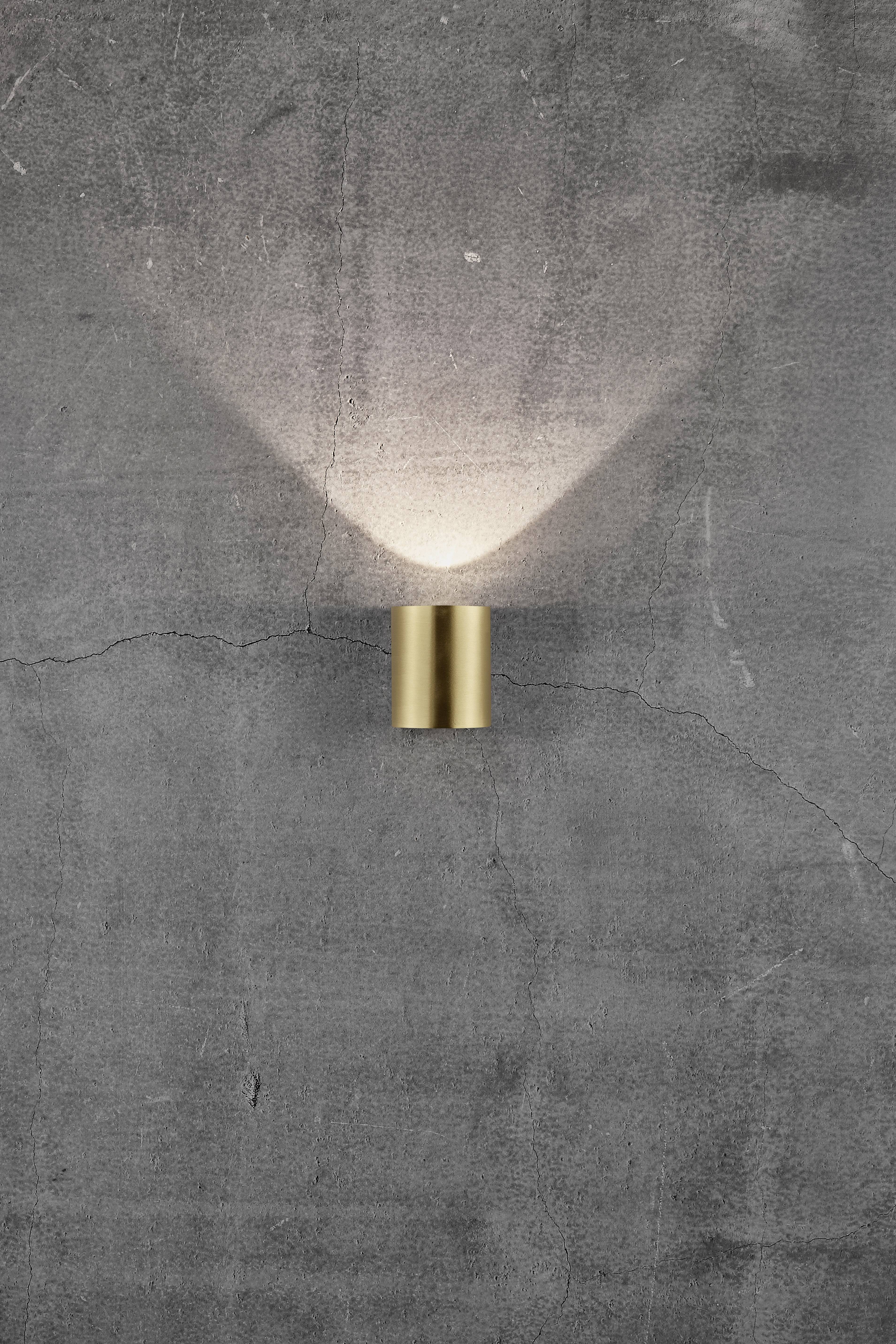 A golden wall light casts bright light upwards against a grey, textured concrete wall with visible cracks.