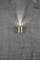 Wall light with a cylindrical, golden body, radiating warm light upwards and downwards, mounted on a grey concrete wall.