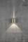A golden wall light casts light cones both upwards and downwards onto a grey concrete wall. The wall has fine cracks.