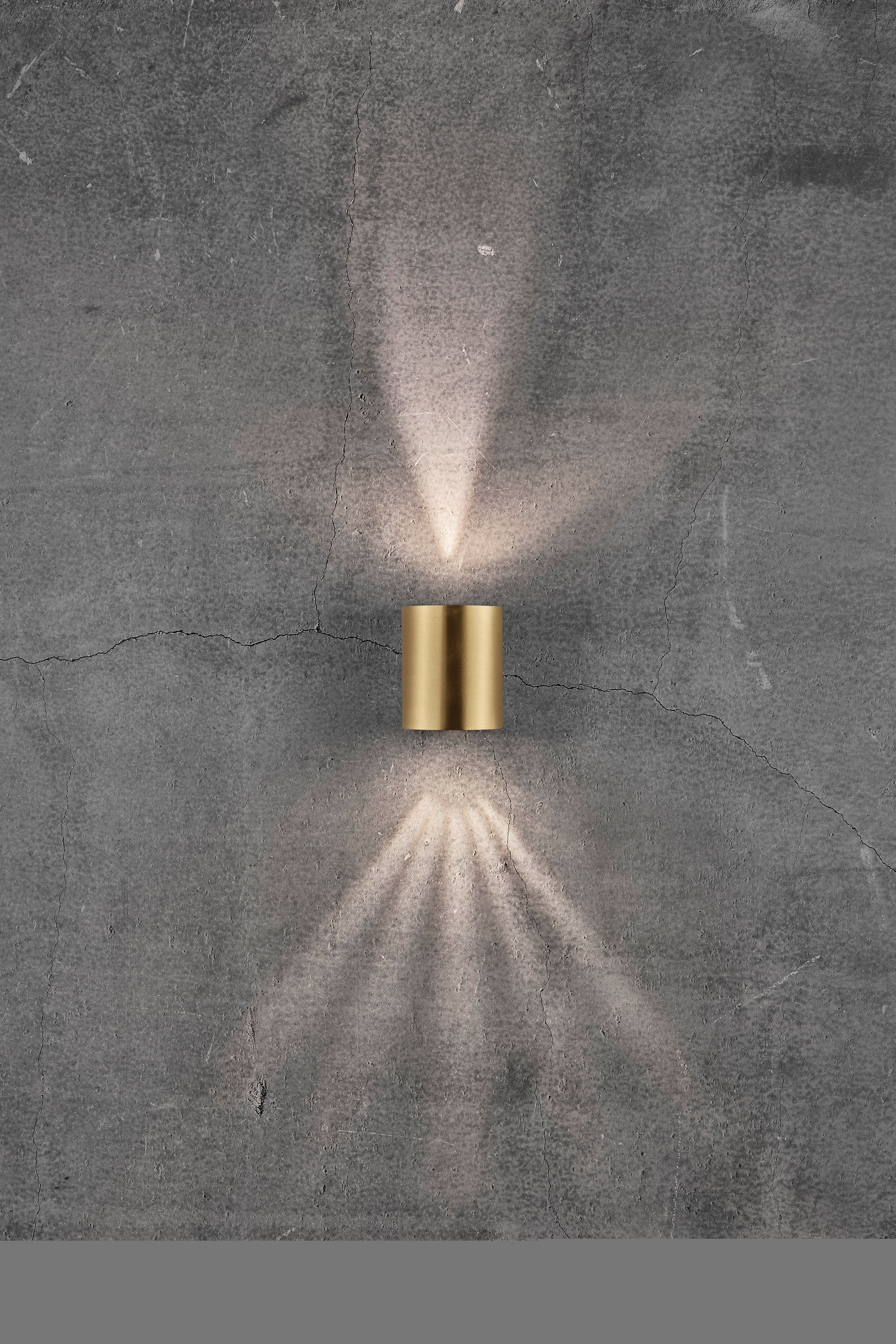 A gold wall light on a grey, textured background, emitting light rays upwards and downwards.