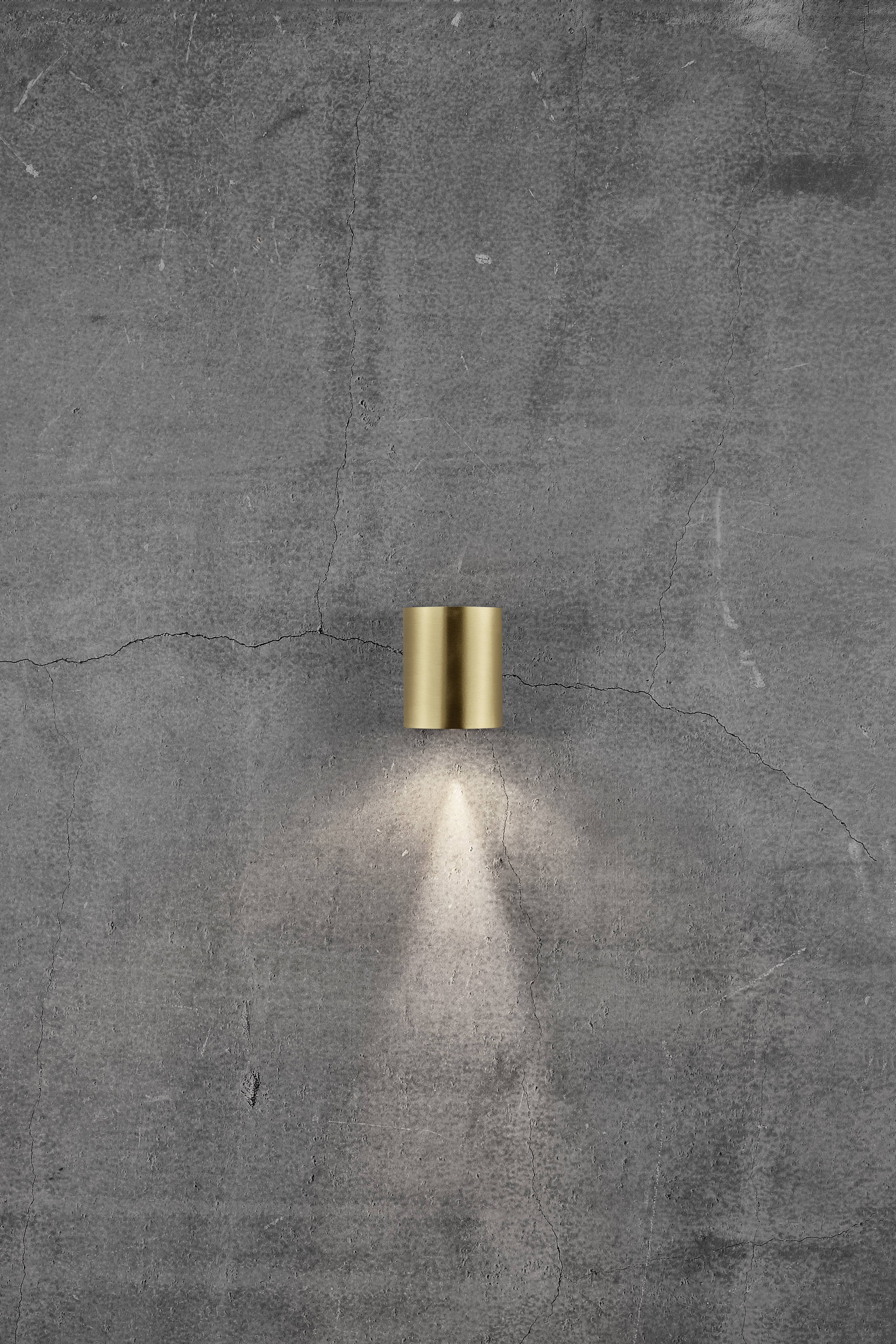 Wall light with golden fitting gleams against a grey, cracked concrete wall.